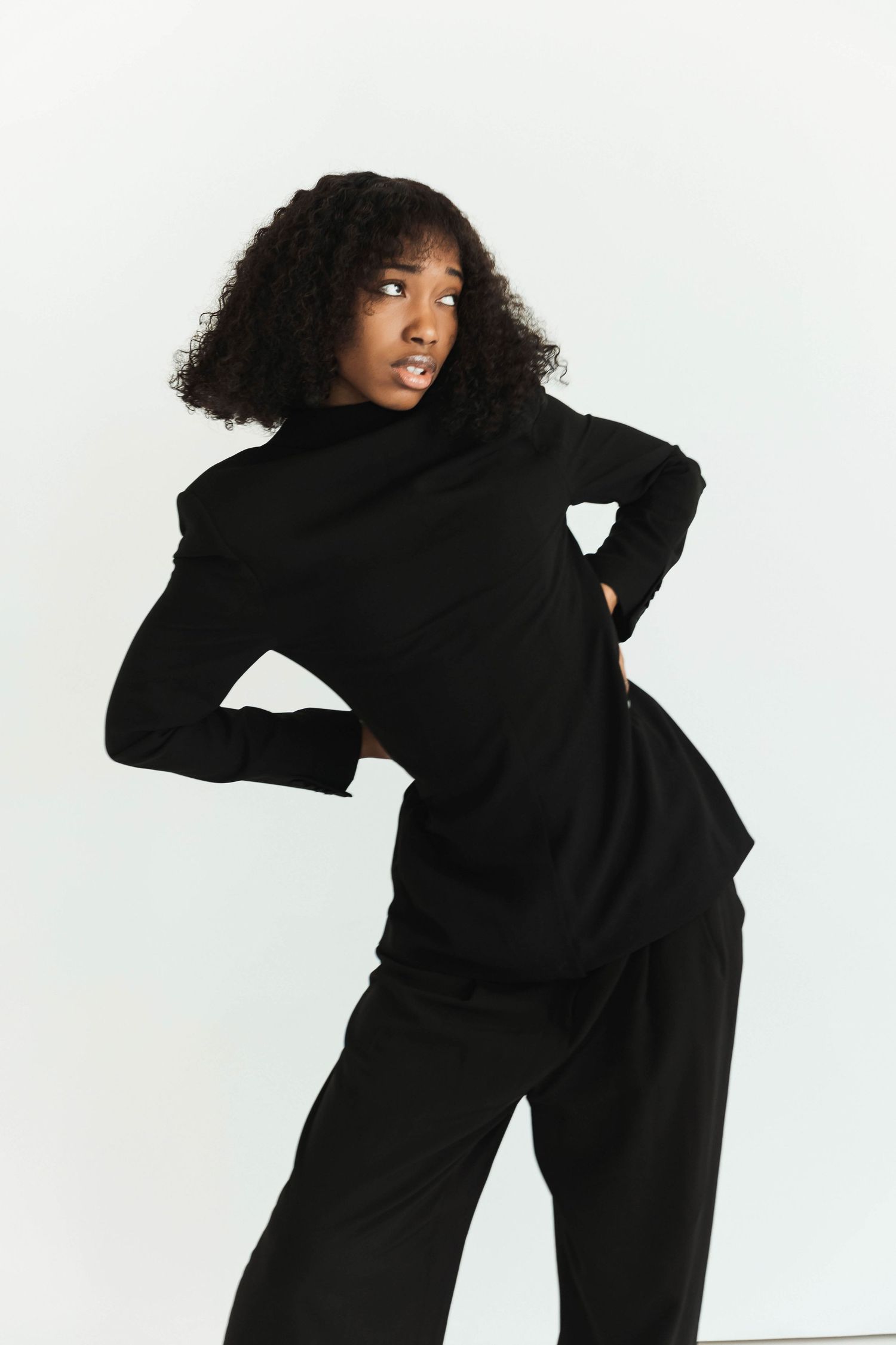 Woman modeling black turtleneck long-sleeve top with wide-leg trousers, back view.