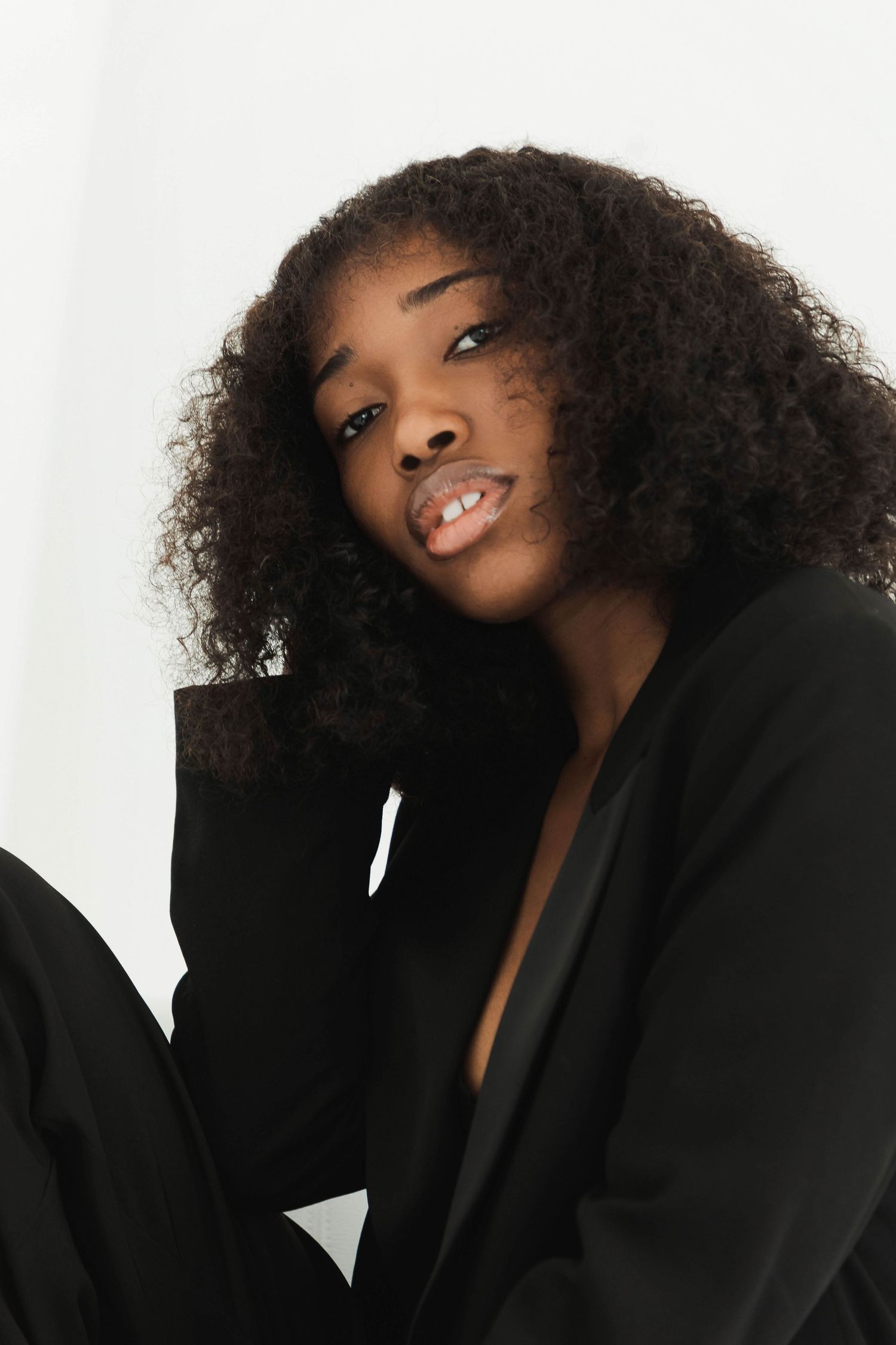 Young Black woman with curly hair wearing a black blazer, smiling softly against a white background.