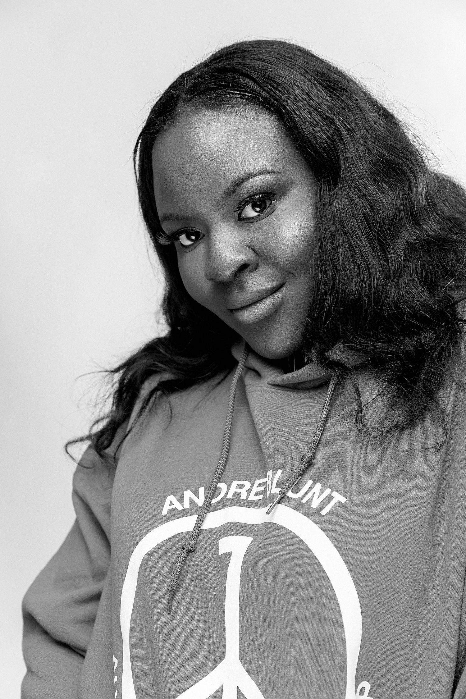 Black and white portrait of a young woman wearing an Andrew Hunt peace sign hoodie, smiling softly at camera.