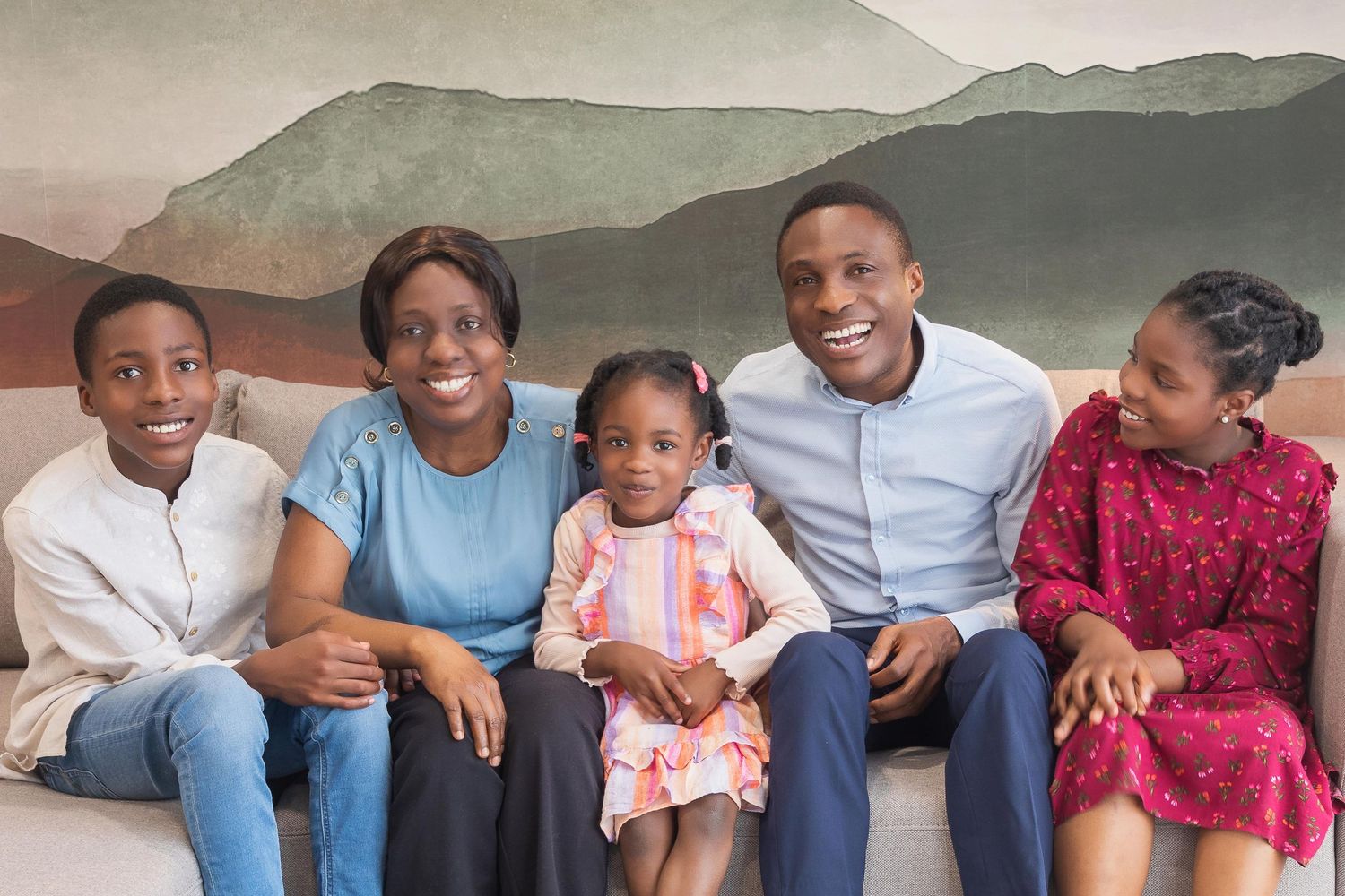 Happy family of five smiling together on a couch, including parents and three children in a warmly decorated room.