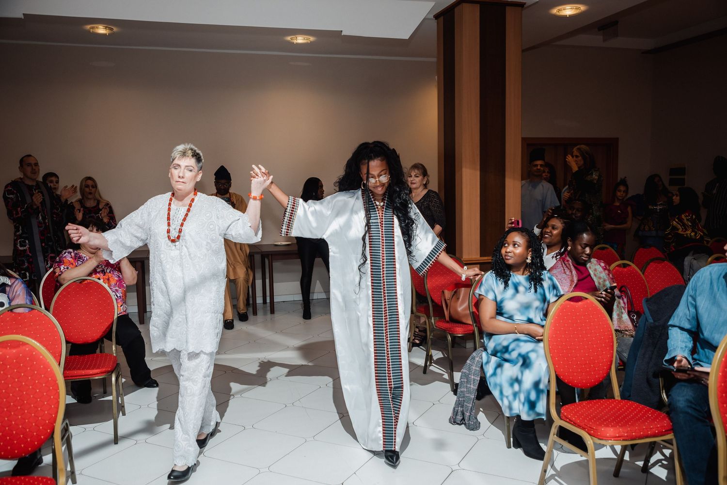 Two women in traditional African attire walk gracefully through a decorated hall during a cultural celebration event.