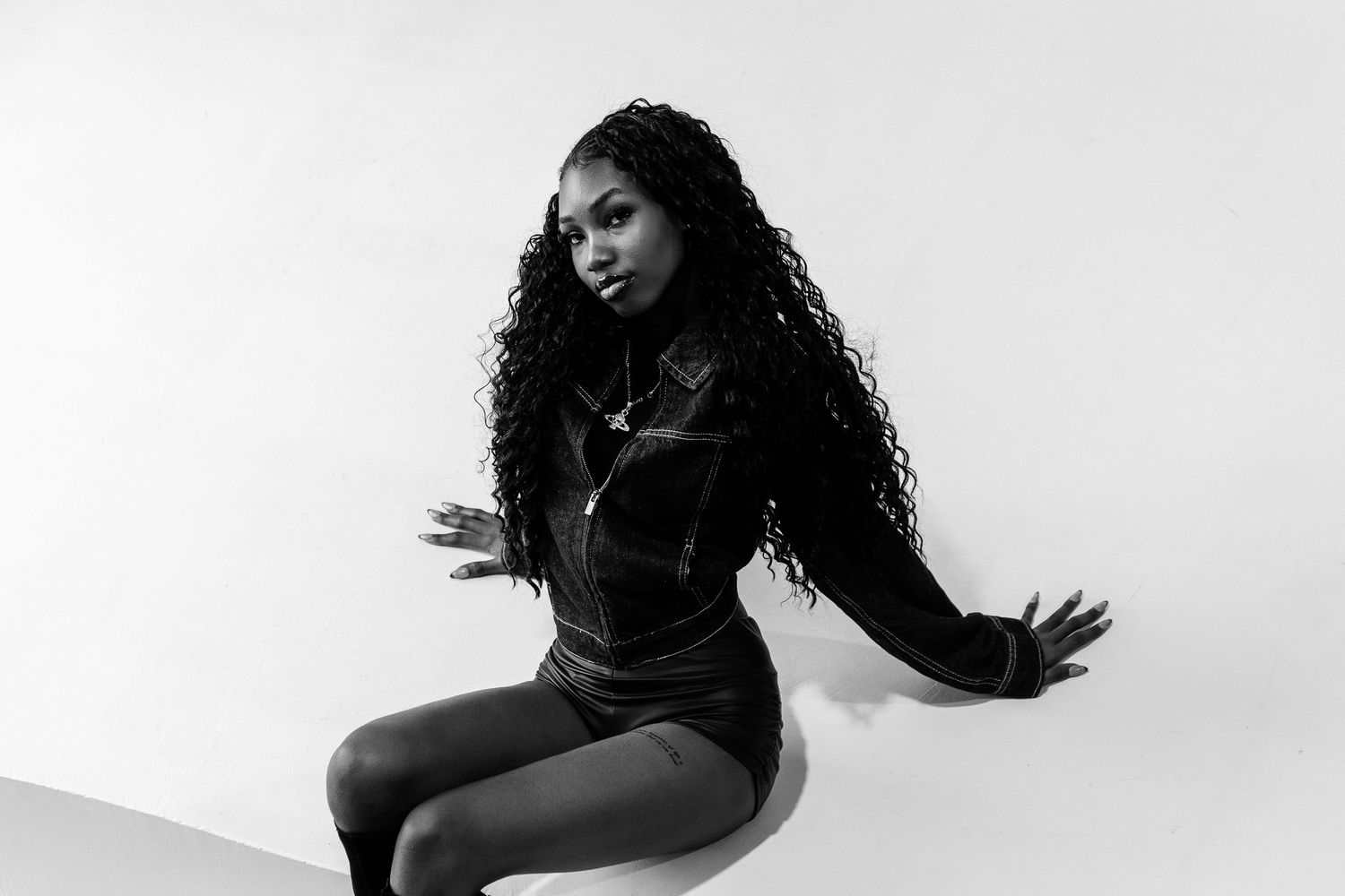Black and white photo of a young woman with long curly hair posing confidently in a dark denim outfit.