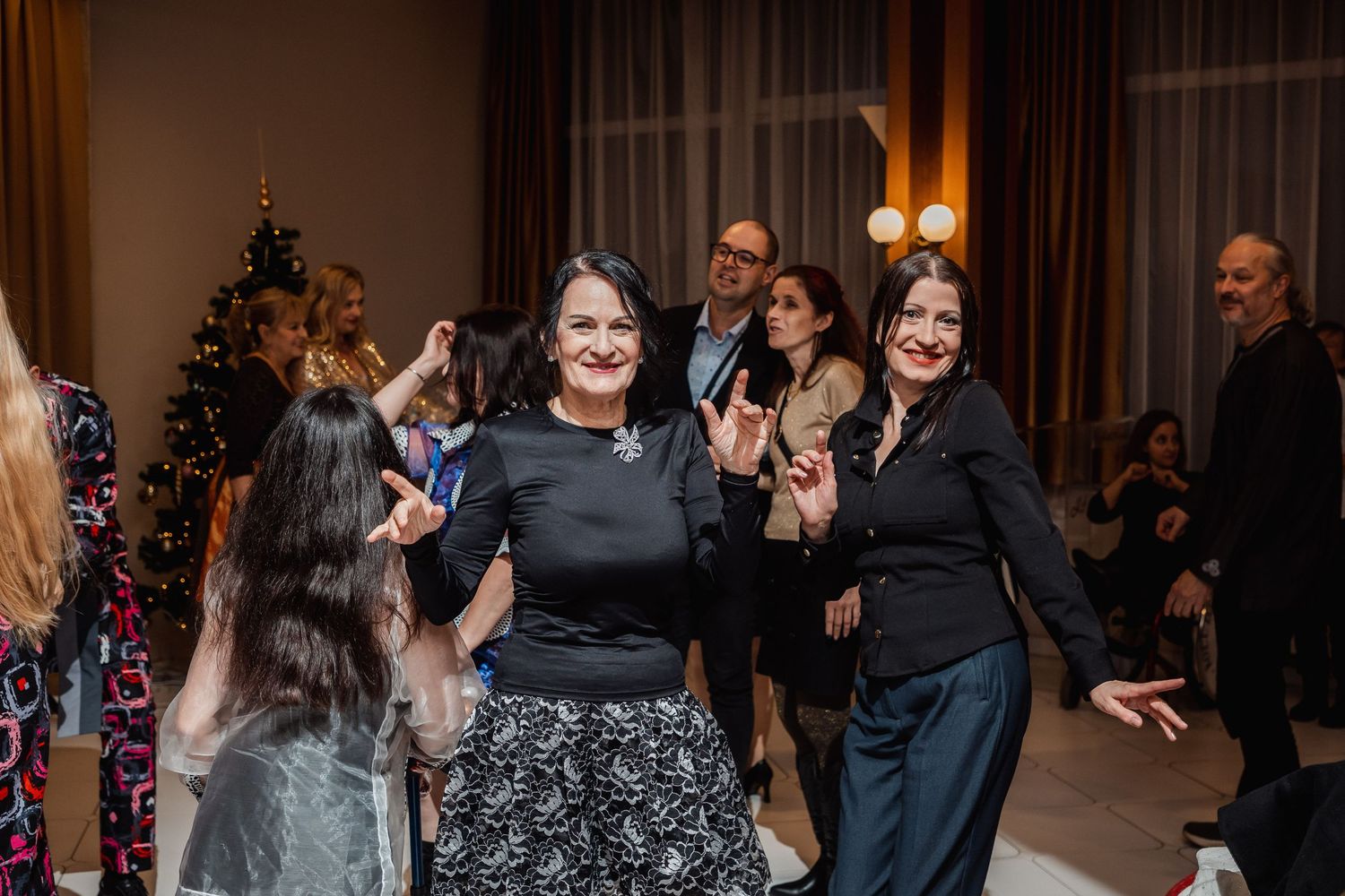 Women dancing joyfully at a festive Christmas party with holiday decorations and guests in background.