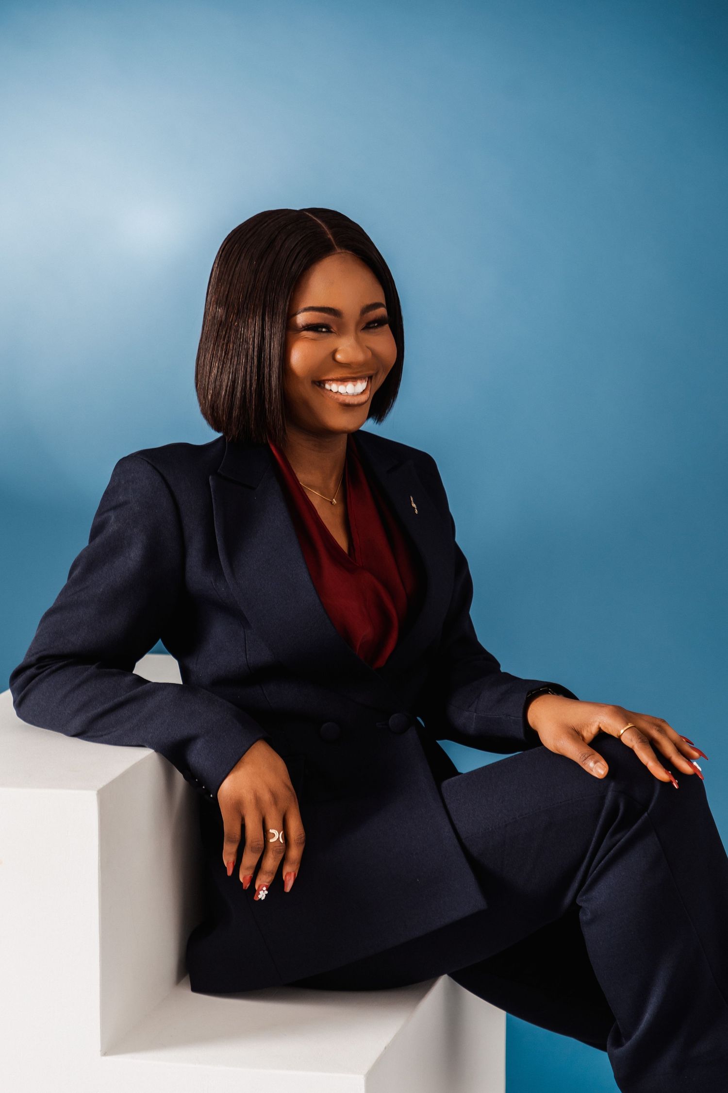 Professional woman in navy suit smiling confidently, seated against a blue background in a polished business portrait.