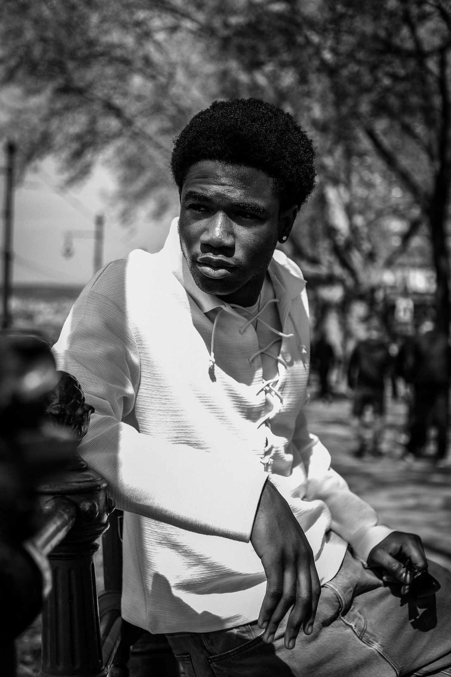 Black and white portrait of a young man with an afro, wearing a white shirt, leaning on a railing outdoors.