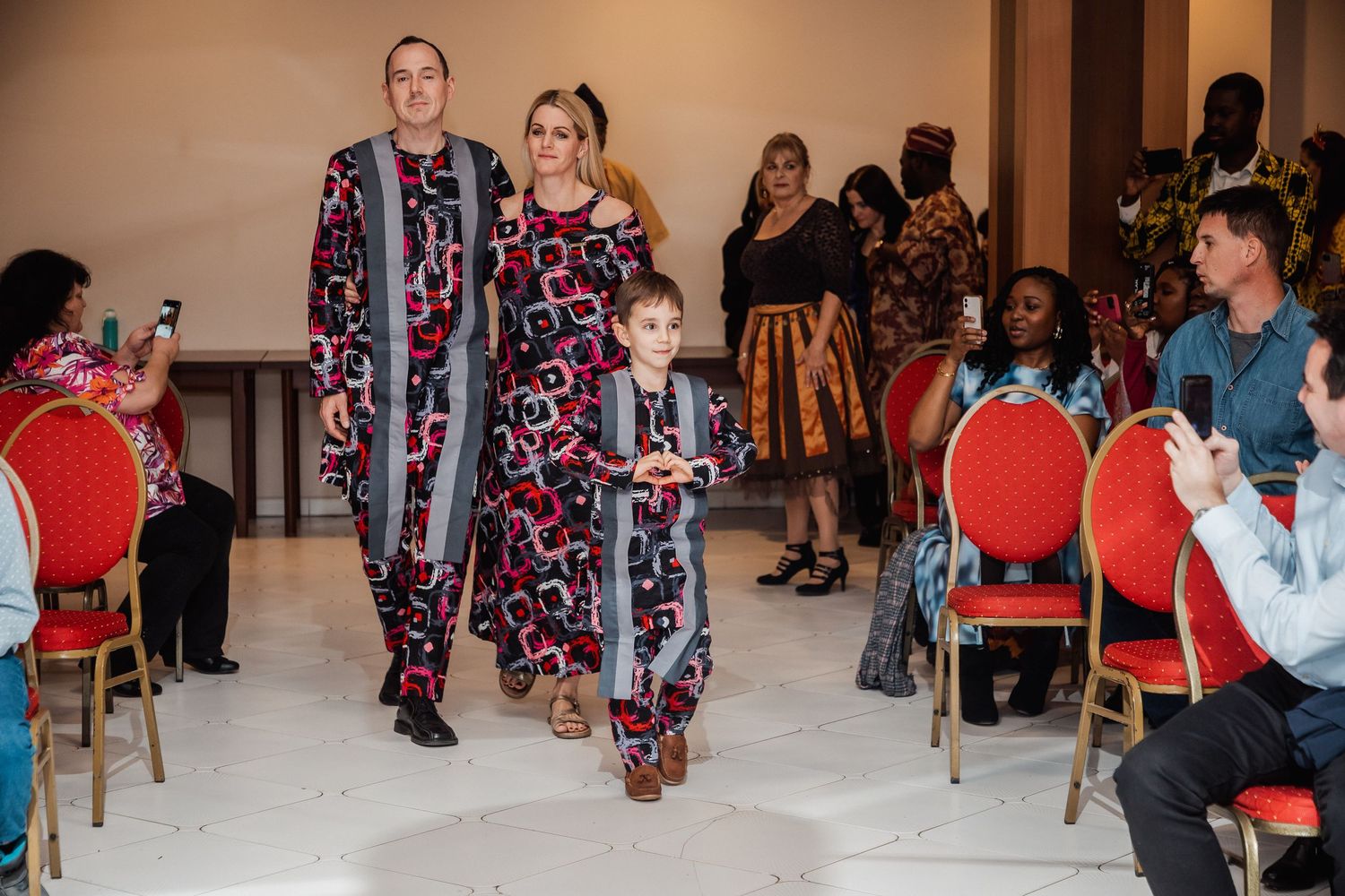 Family of three in matching patterned outfits walks the runway at a multicultural fashion show event.