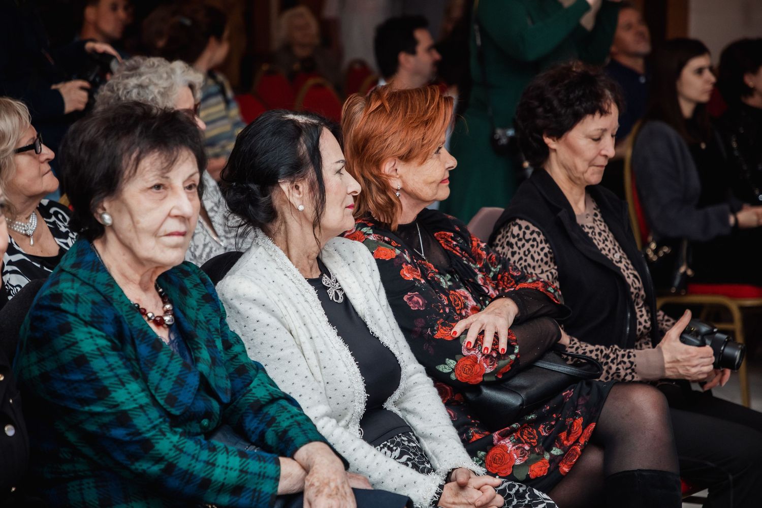Group of senior women sitting together smiling and laughing at an indoor social gathering event.