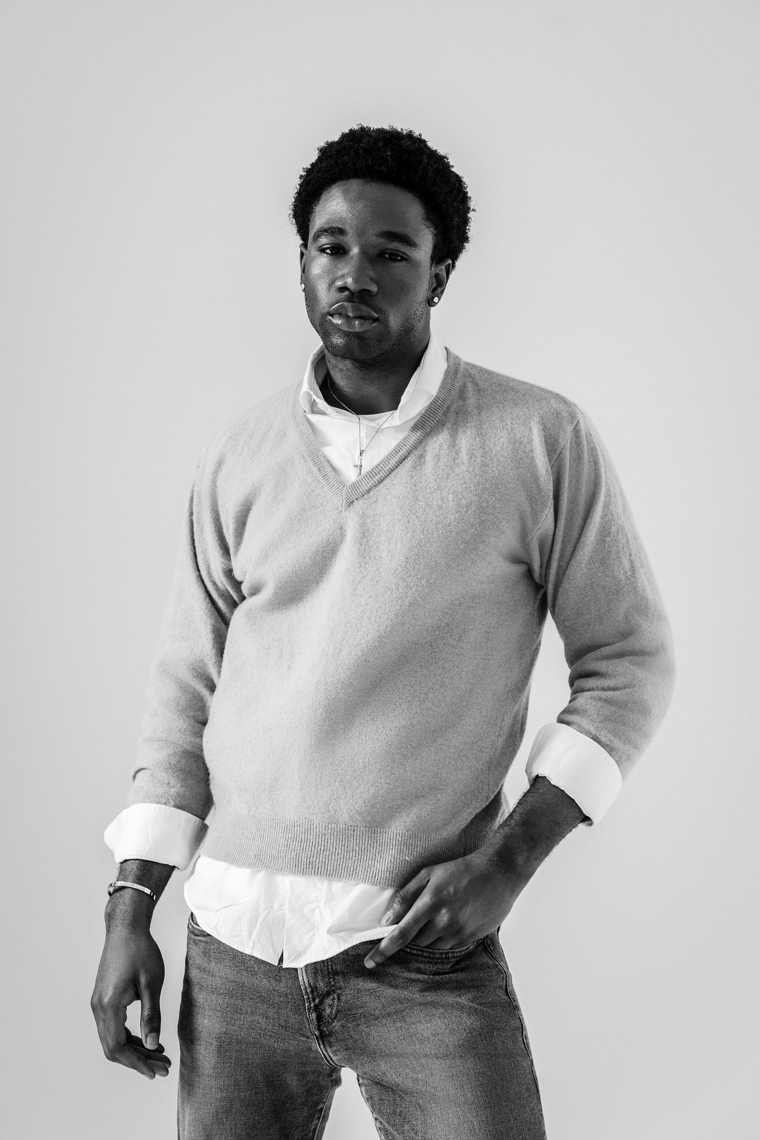 Black and white portrait of a young man in a sweater and jeans posing confidently against a light background.