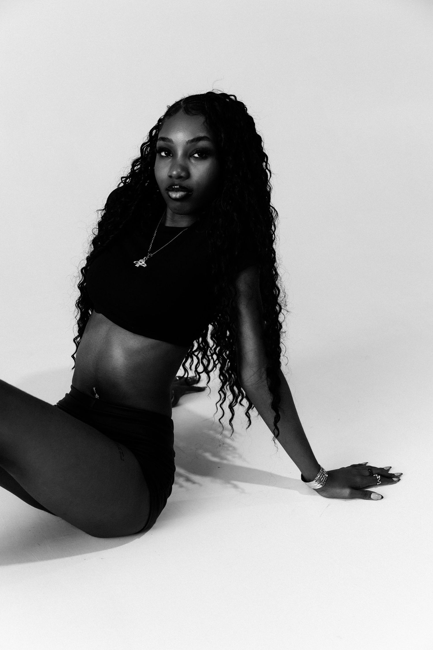 Black and white portrait of a young woman with long curly hair sitting gracefully in a studio setting.