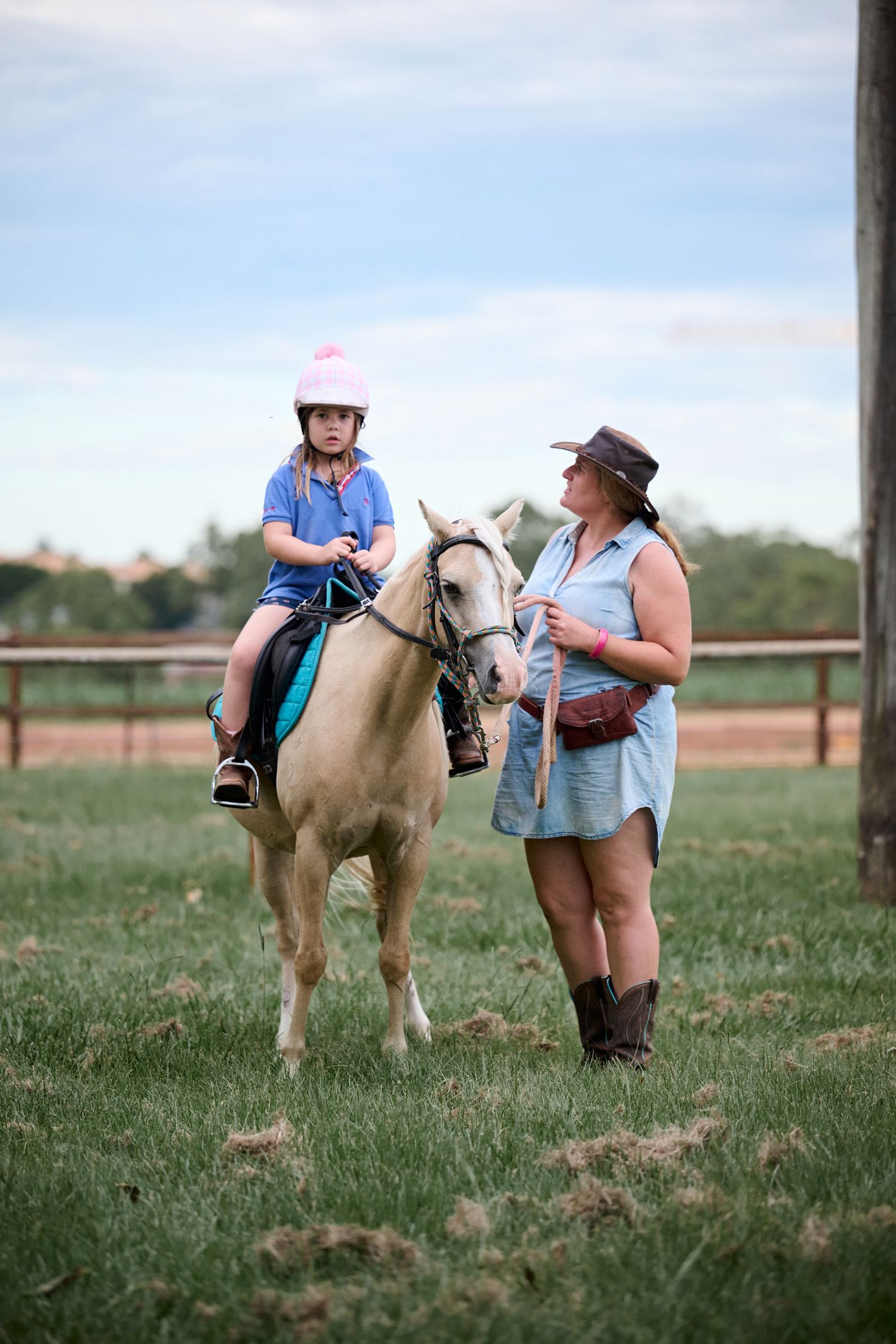 A palomino pony and riders enjoy outdoor horseback riding lessons in a grassy paddock on a sunny day.