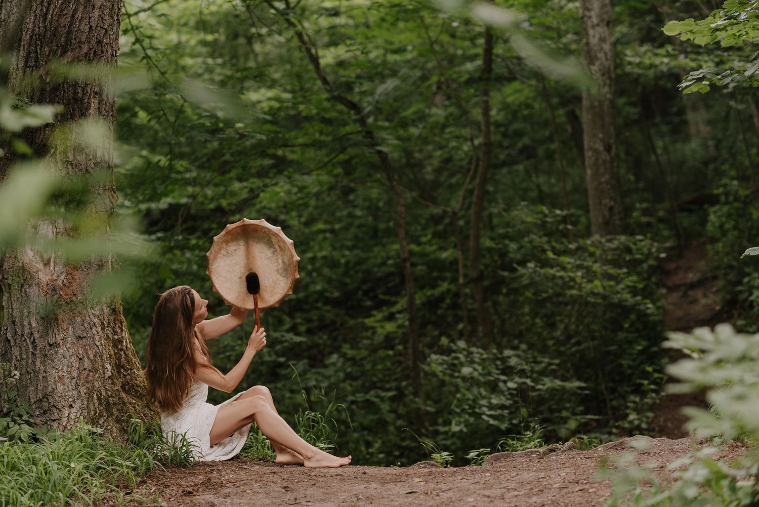 Person sitting on forest path holding tambourine in dreamy woodland setting.