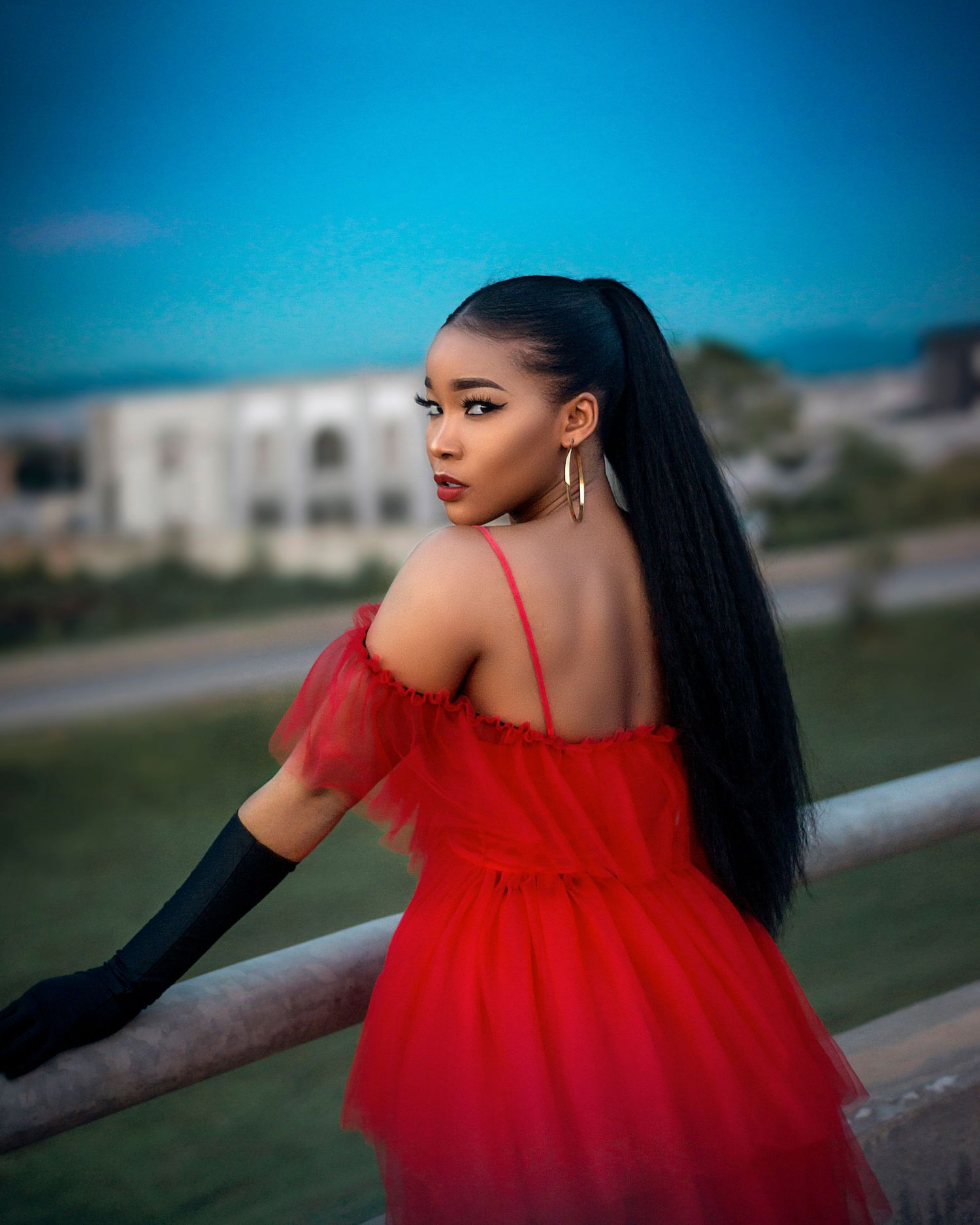 An actress posing in a striking red dress along a walkway, with a stylish and elegant ambiance.
