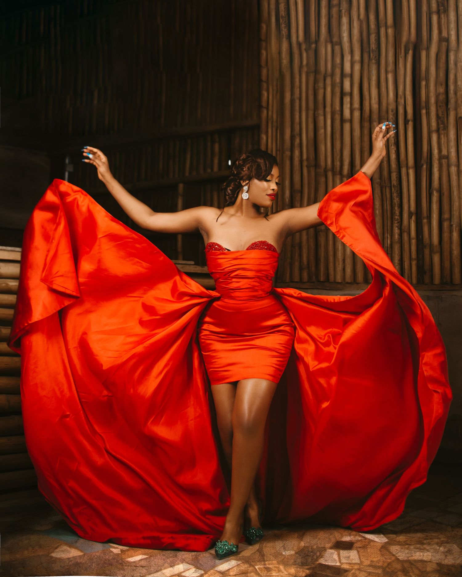 A lady in a red dress stylishly tossing the flair of her dress into the air while striking a pose.