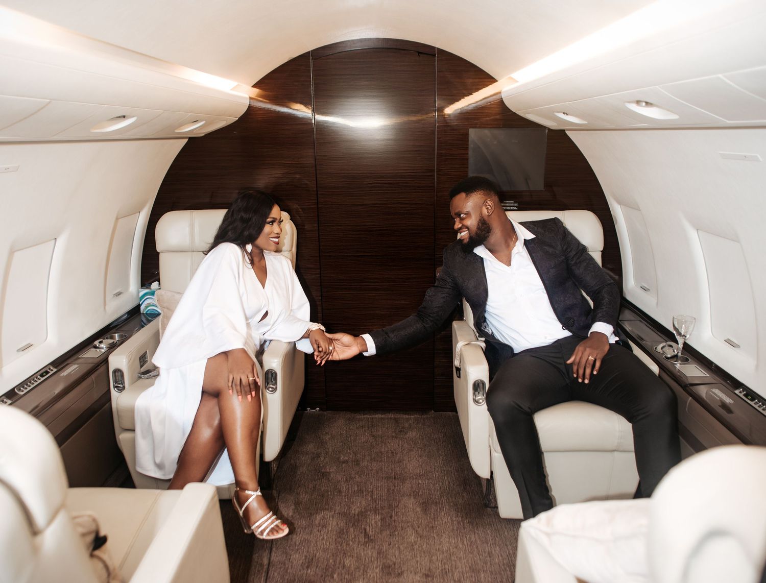A pre-wedding photo of a couple holding hands, seated inside the luxurious interior of a private jet.