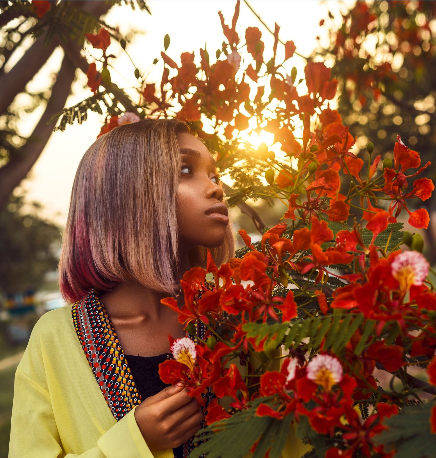 A portrait of a young model standing in front of red flowers.