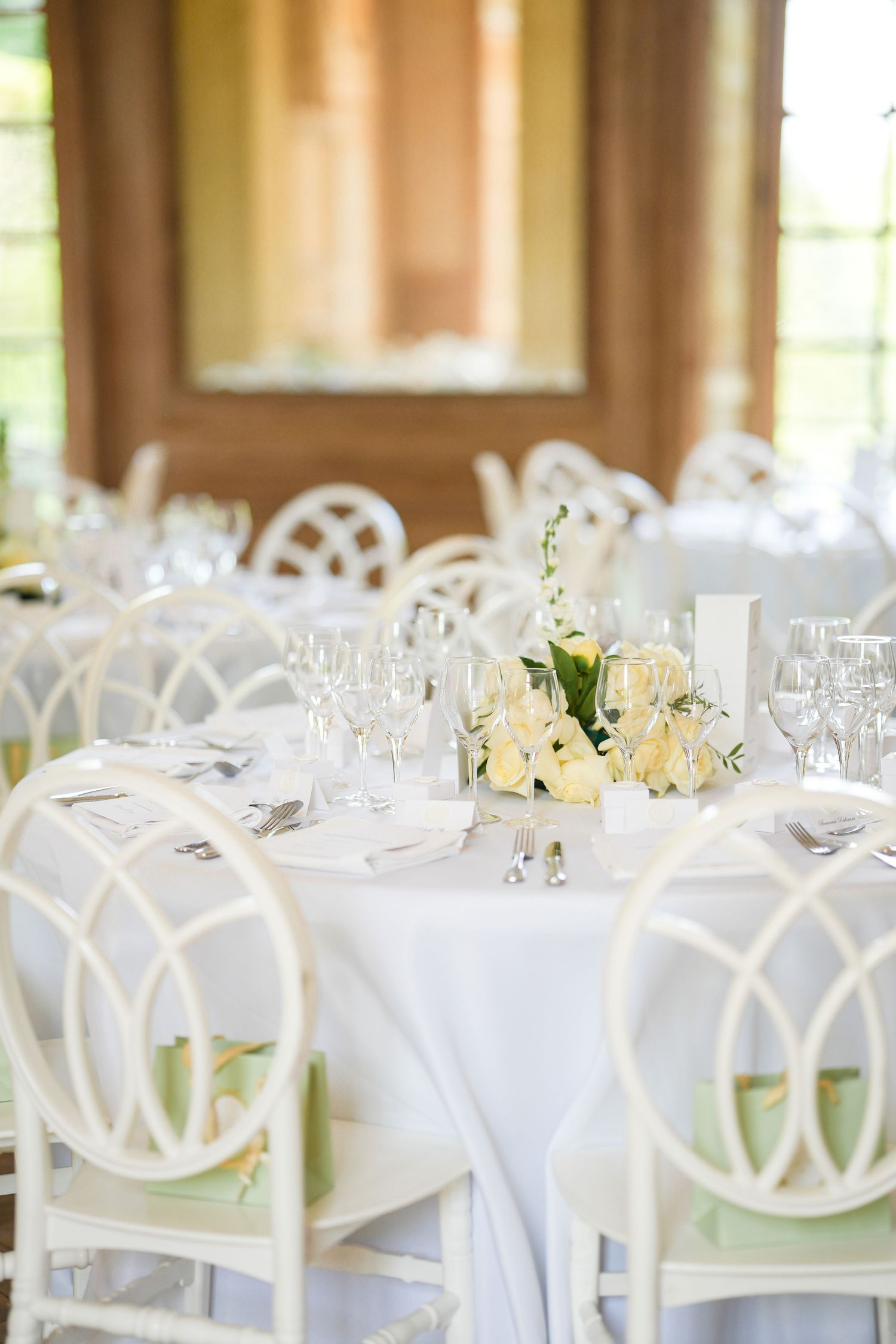 Elegant wedding reception table setting with white tablecloth, lattice-back chairs and pale yellow floral centerpiece.