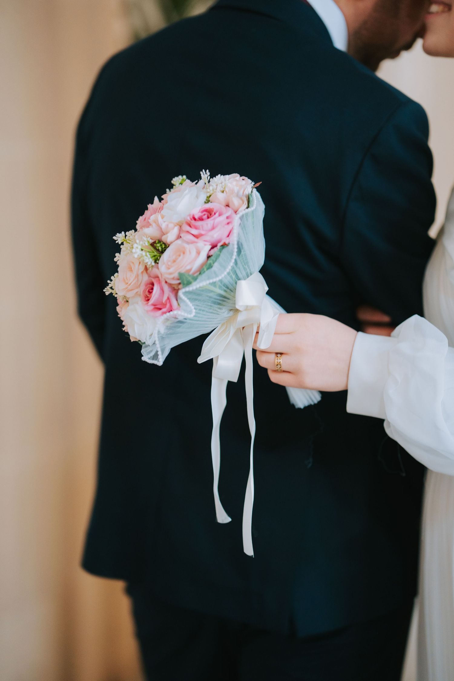 A close-up of a bridal bouquet with pink roses and white flowers being held against a dark suit jacket.