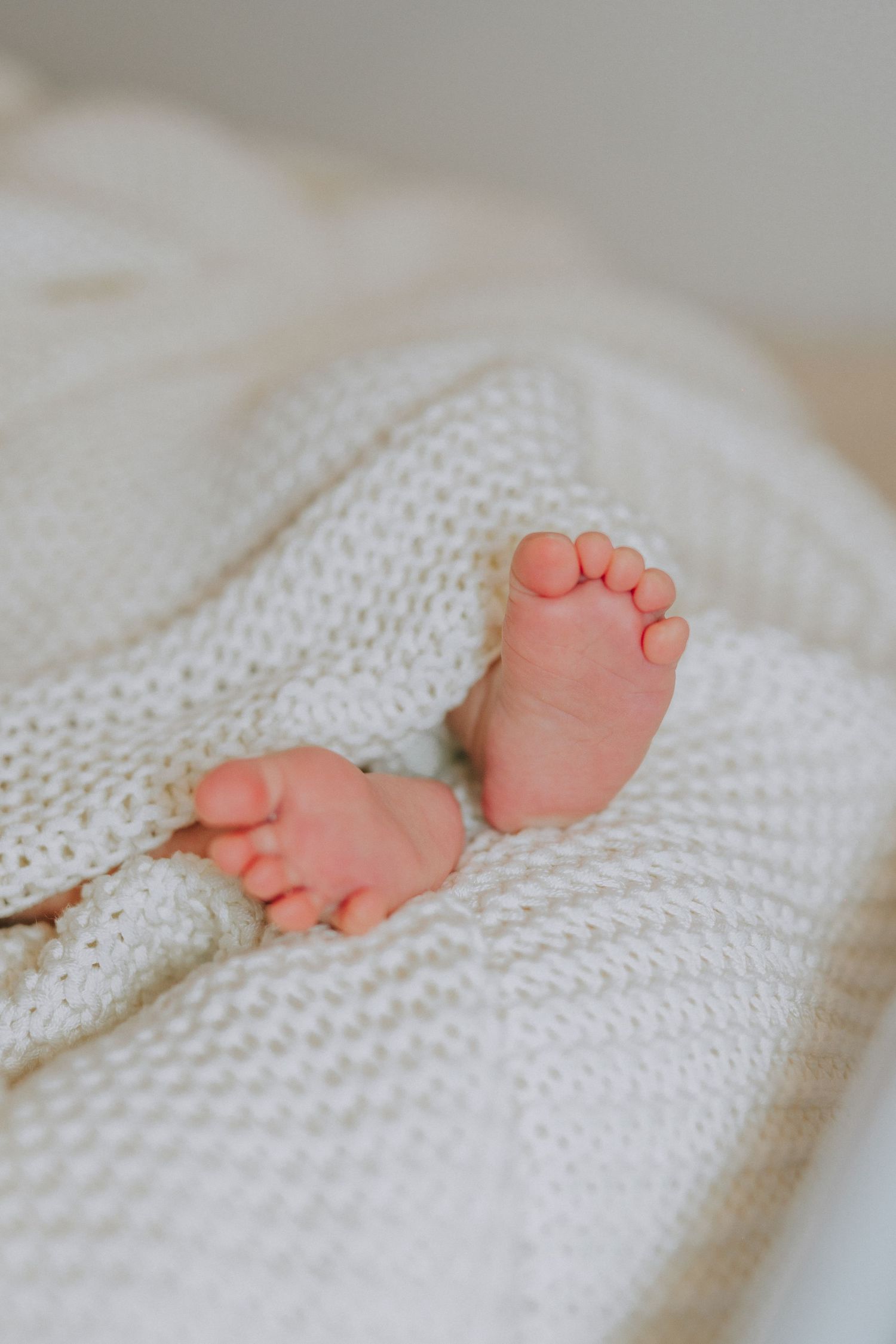 Tiny newborn baby feet resting on a cozy white knitted blanket.