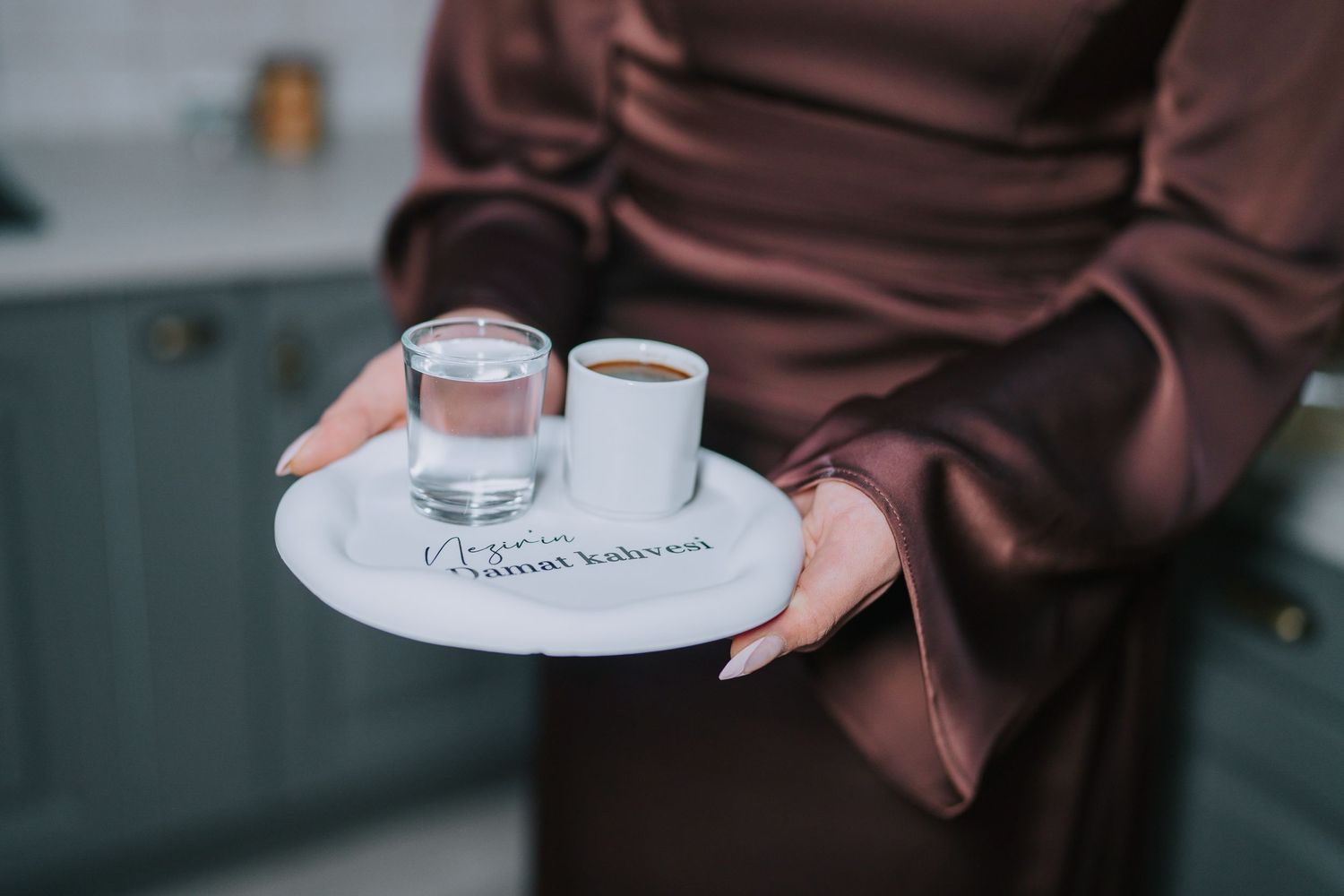 A white serving tray with two small drinks being held by hands in brown sleeves.