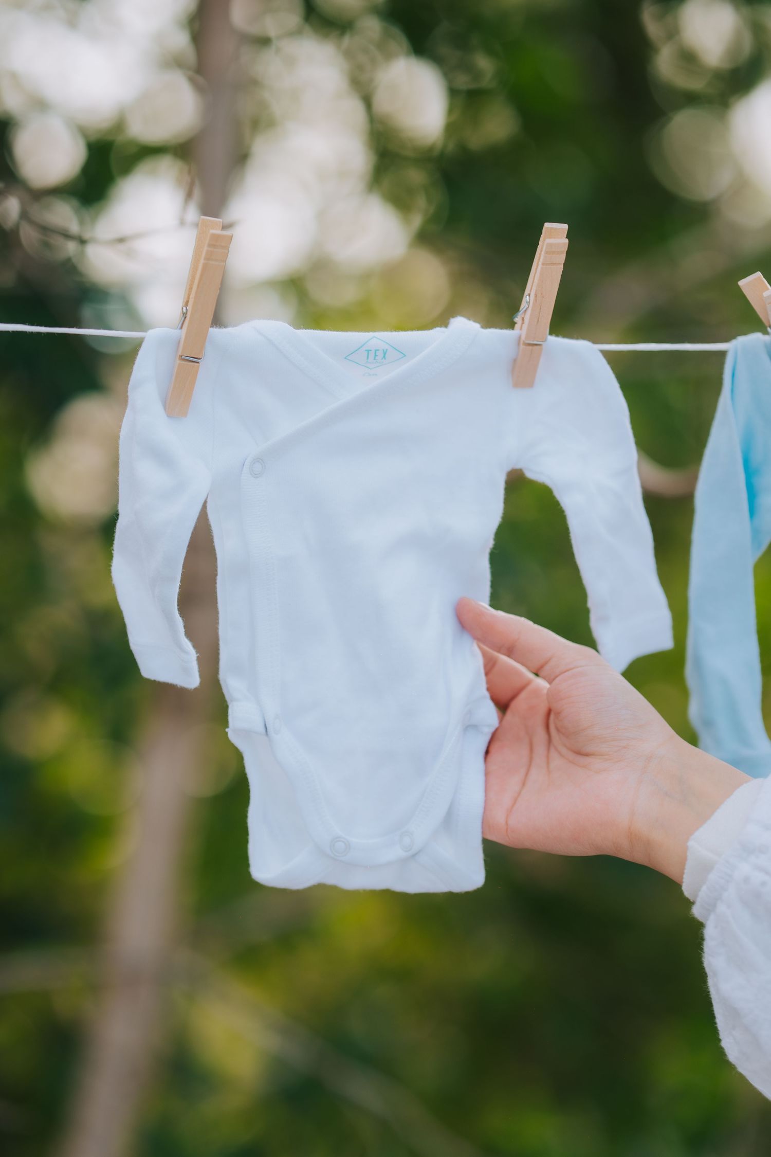 White baby onesie hanging on clothesline with wooden clothespins.