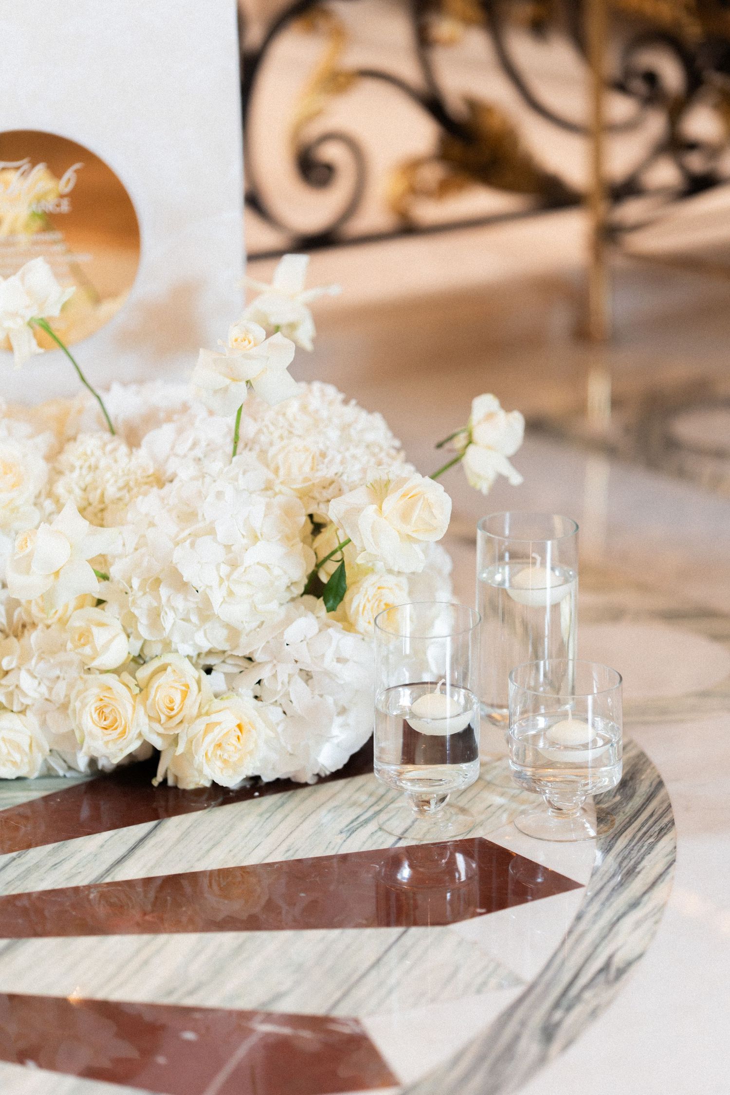 Elegant table decor features white roses and hydrangeas in a bouquet next to glass votives on a modern marble tray.