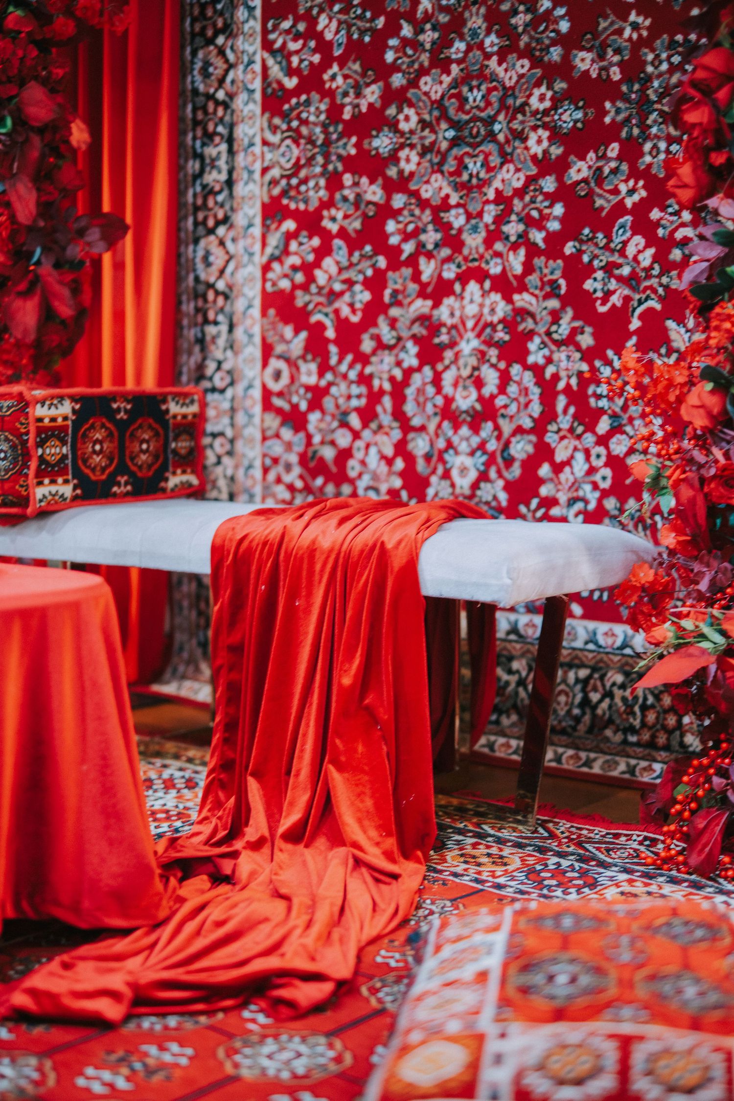 Elegant red wedding decor setup with floral arrangements and draped fabric against patterned backdrop.