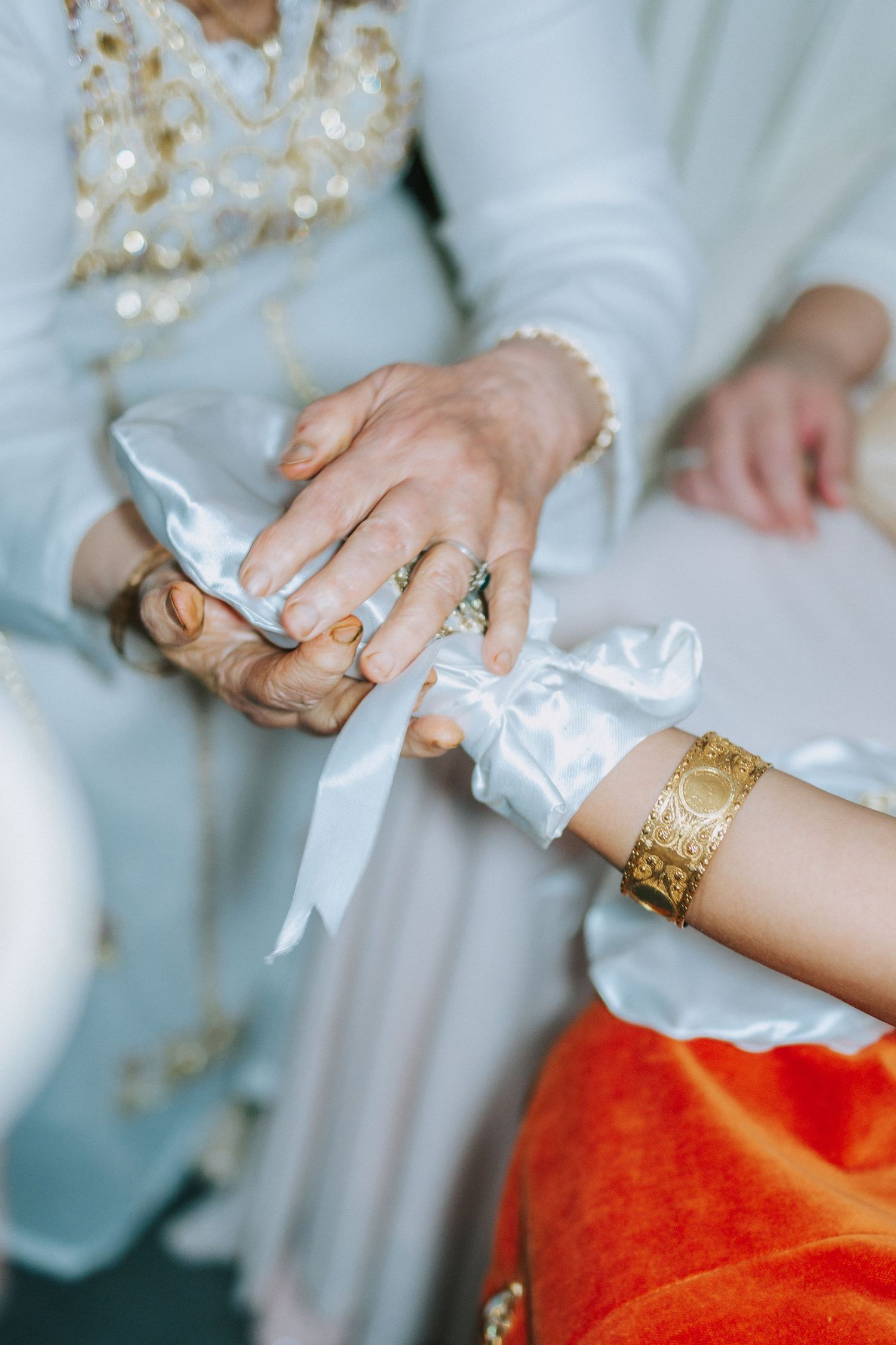 Hands tying white ribbon with decorative gold bangles in traditional ceremony.