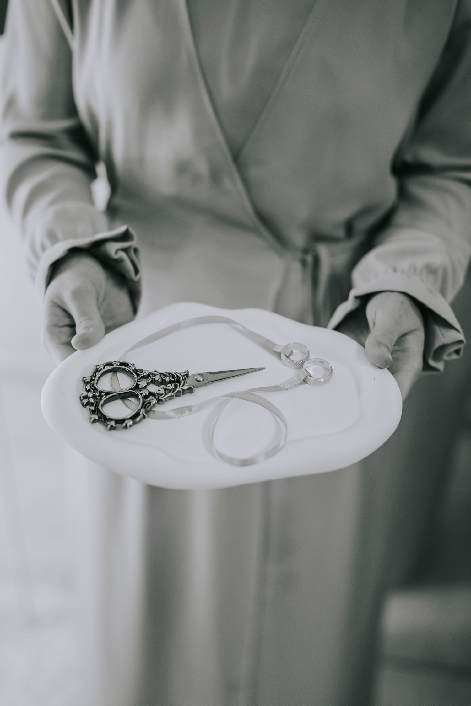 Ornate vintage scissors displayed on a white plate held by hands in a light-colored garment.
