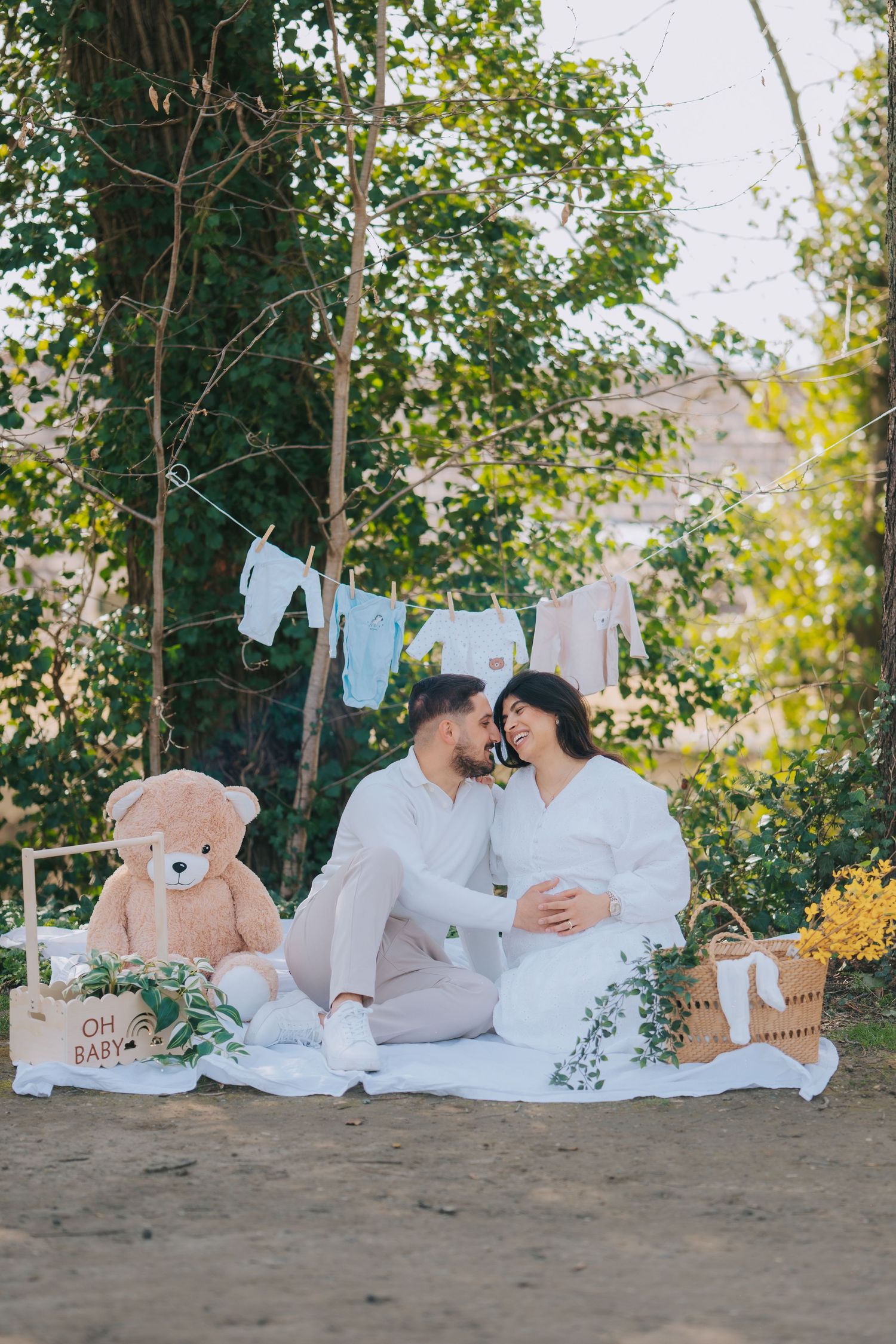 Baby-themed outdoor photoshoot with white clothes, teddy bear and hanging baby items.