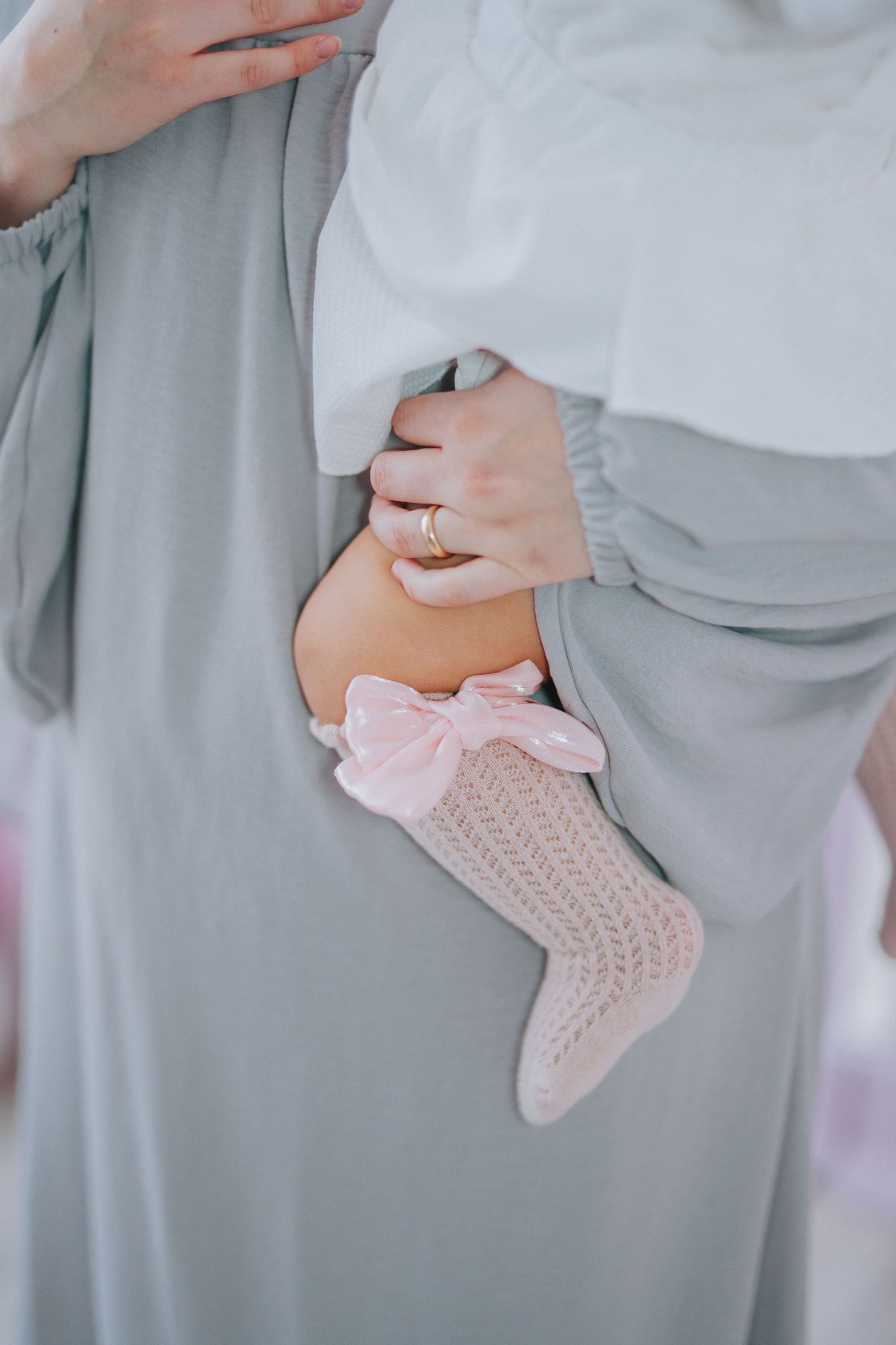 Detail shot of pink knit socks and ring against grey fabric background.