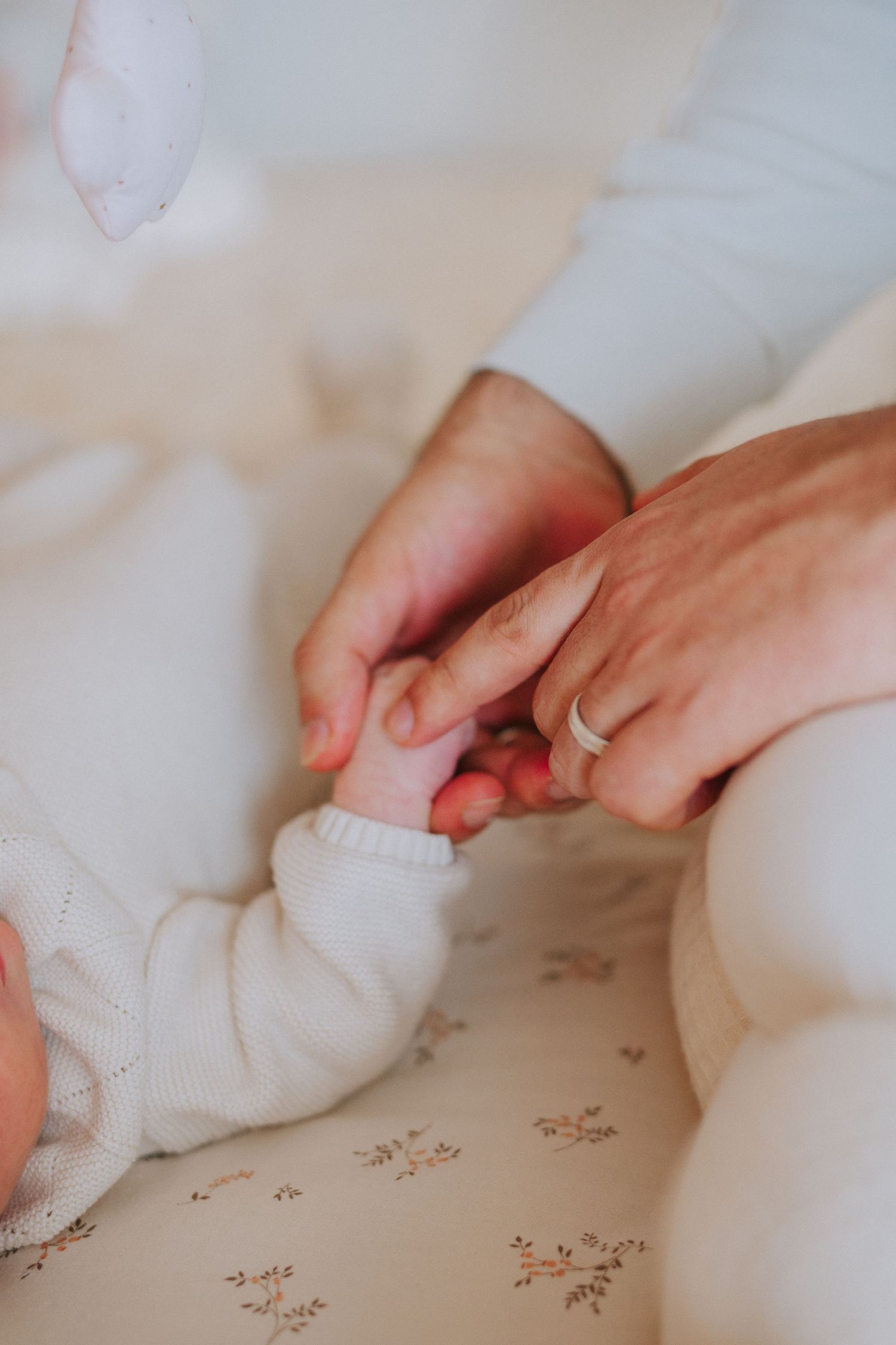 Gentle hands holding small fingers against white patterned fabric.