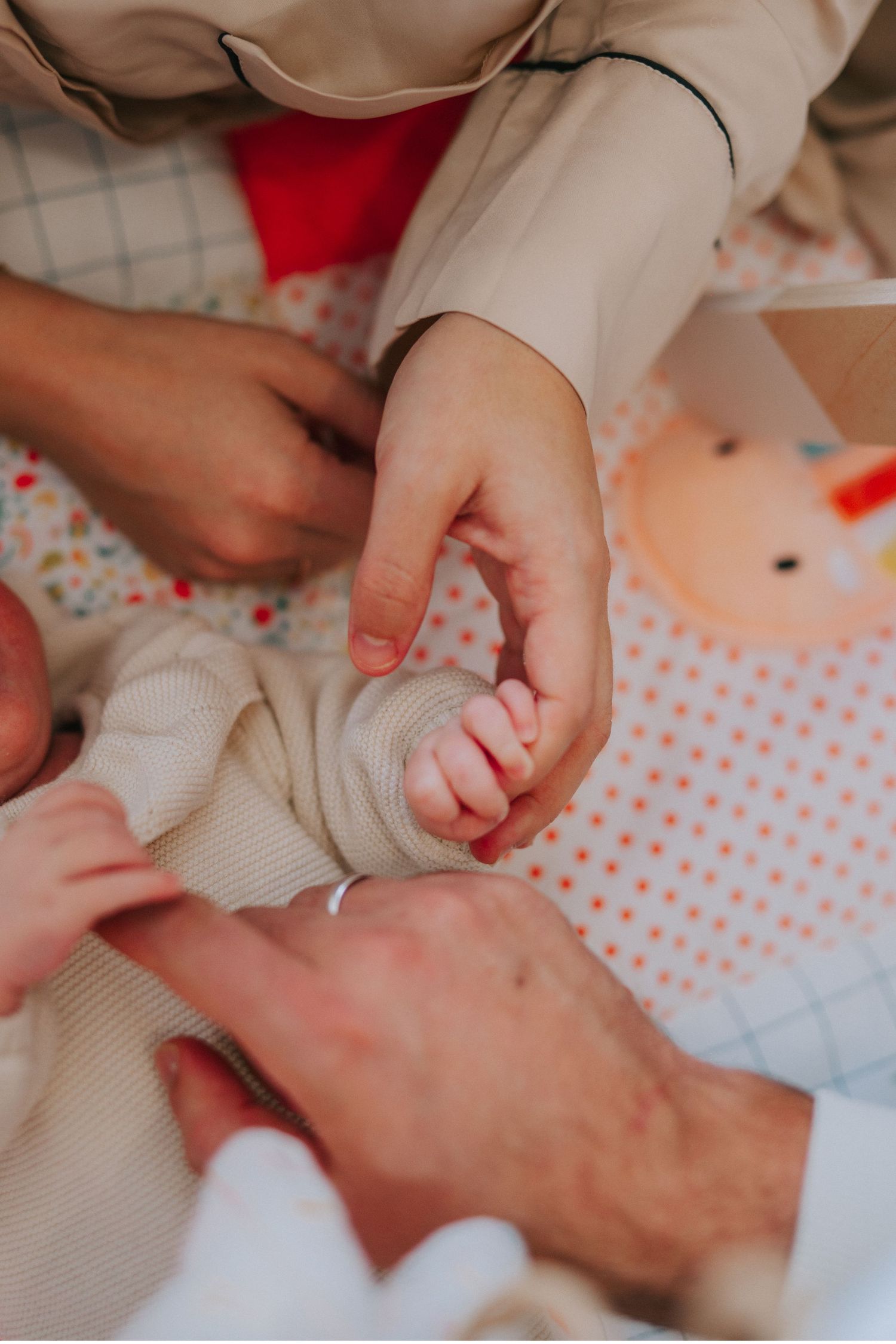 Close-up shot of hands gently holding a newborn baby's tiny foot wrapped in cream-colored fabric.