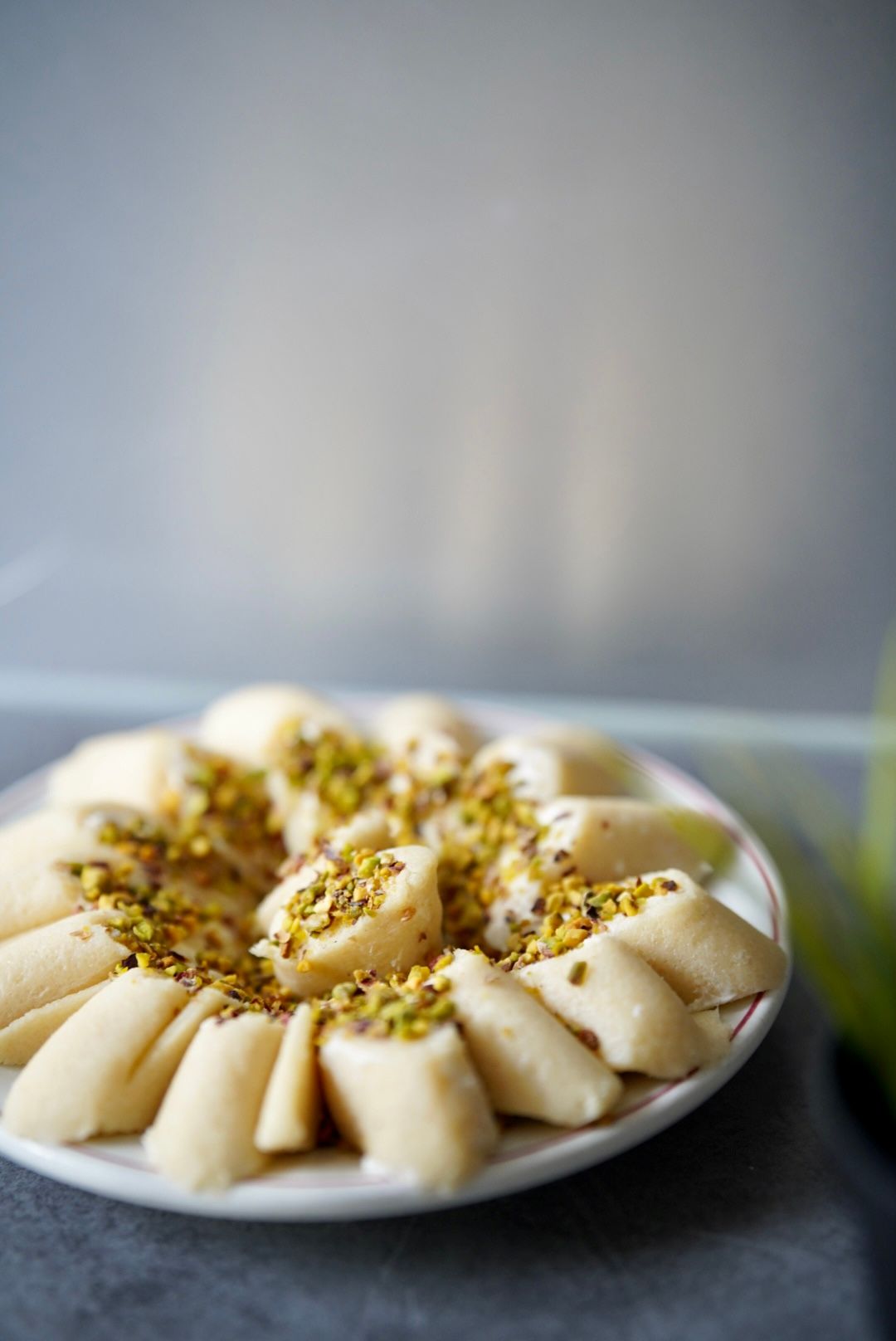 Elegant flower-shaped Middle Eastern dessert topped with crushed pistachios on a white plate.