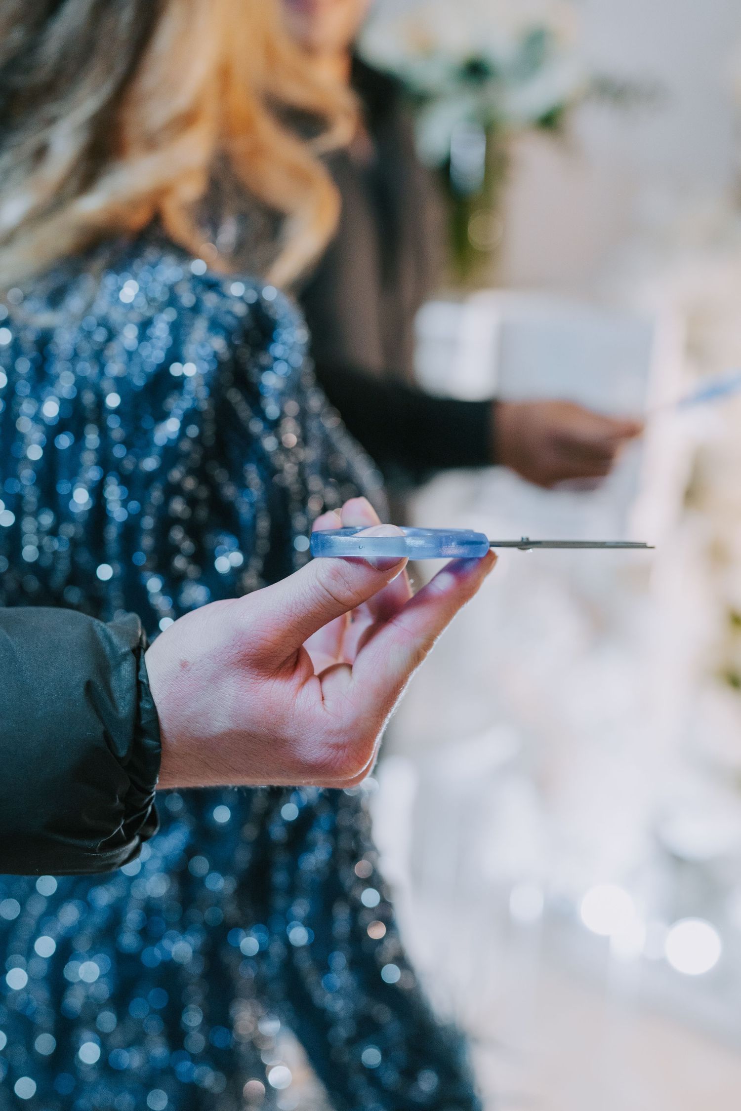 Hand holding a thin pen against a background of sparkly blue fabric.