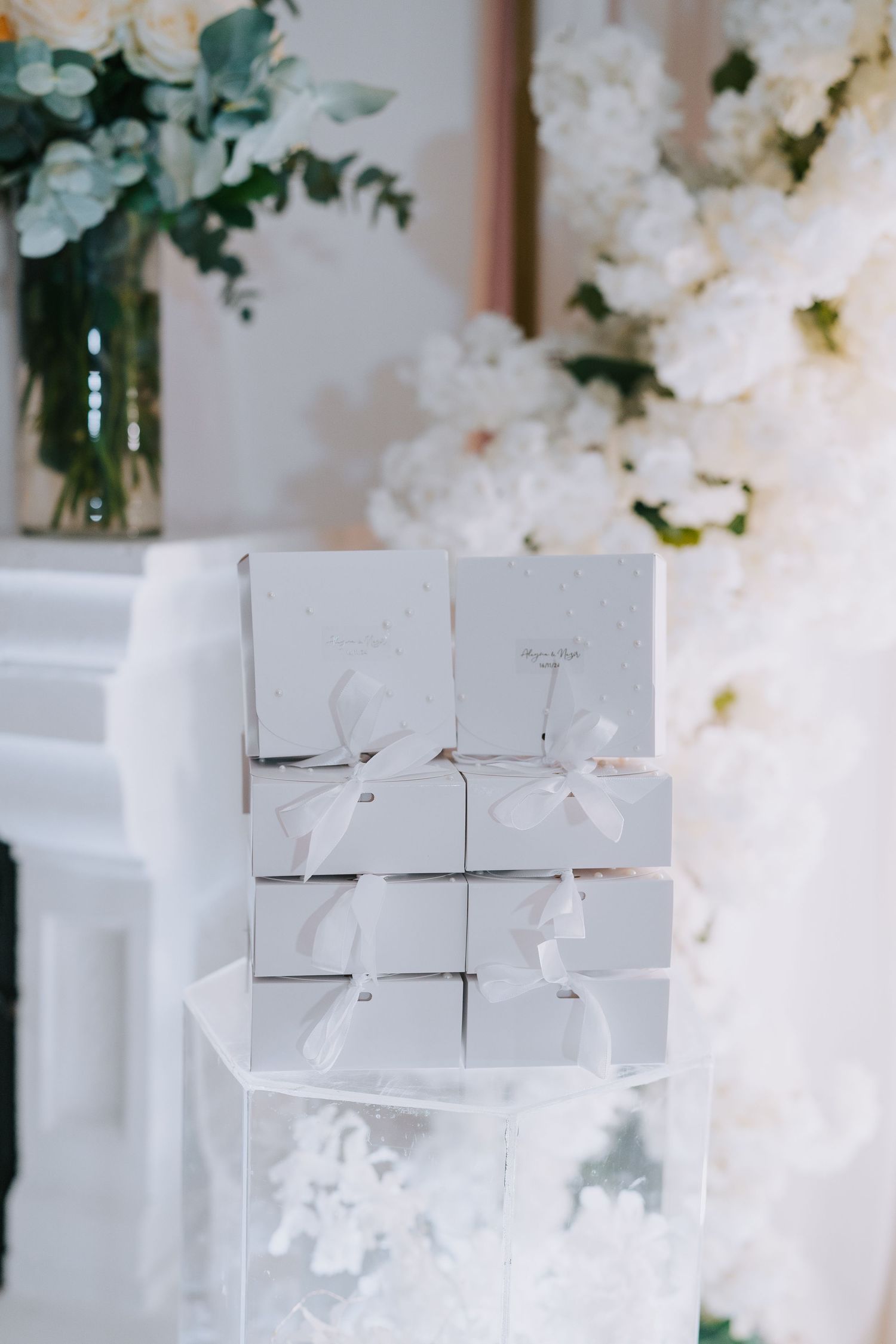 White gift boxes stacked on a mantle with floral arrangements in the background.