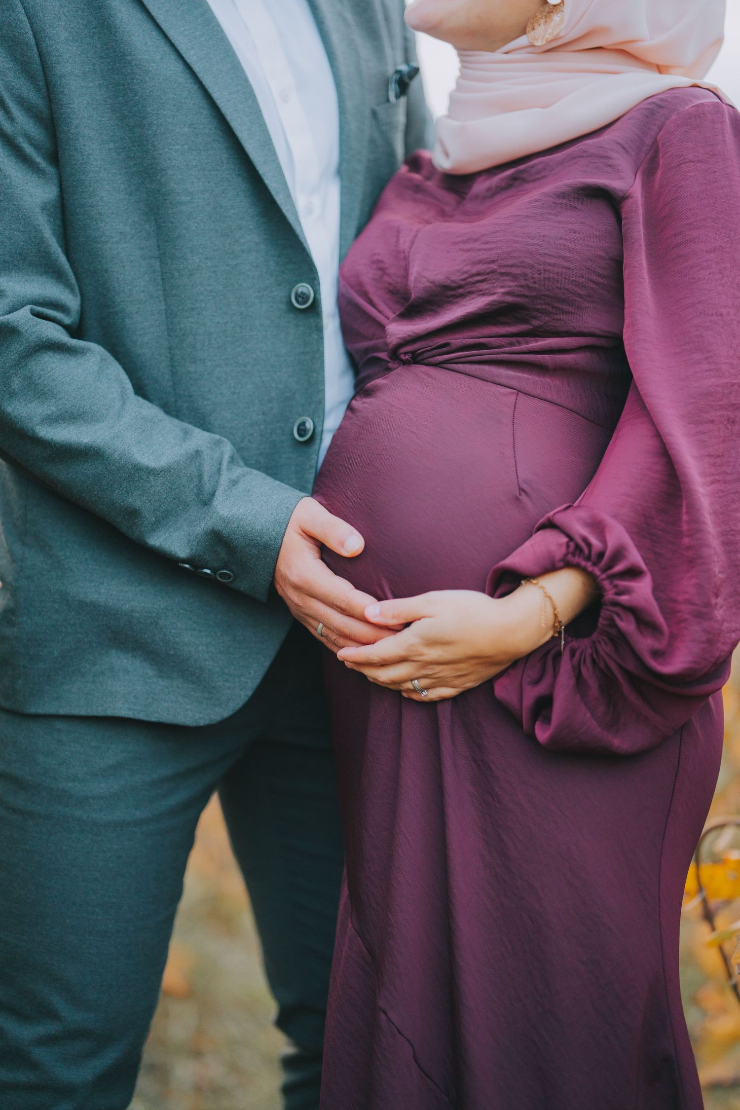 Close-up of hands resting on a burgundy maternity dress against formal attire.