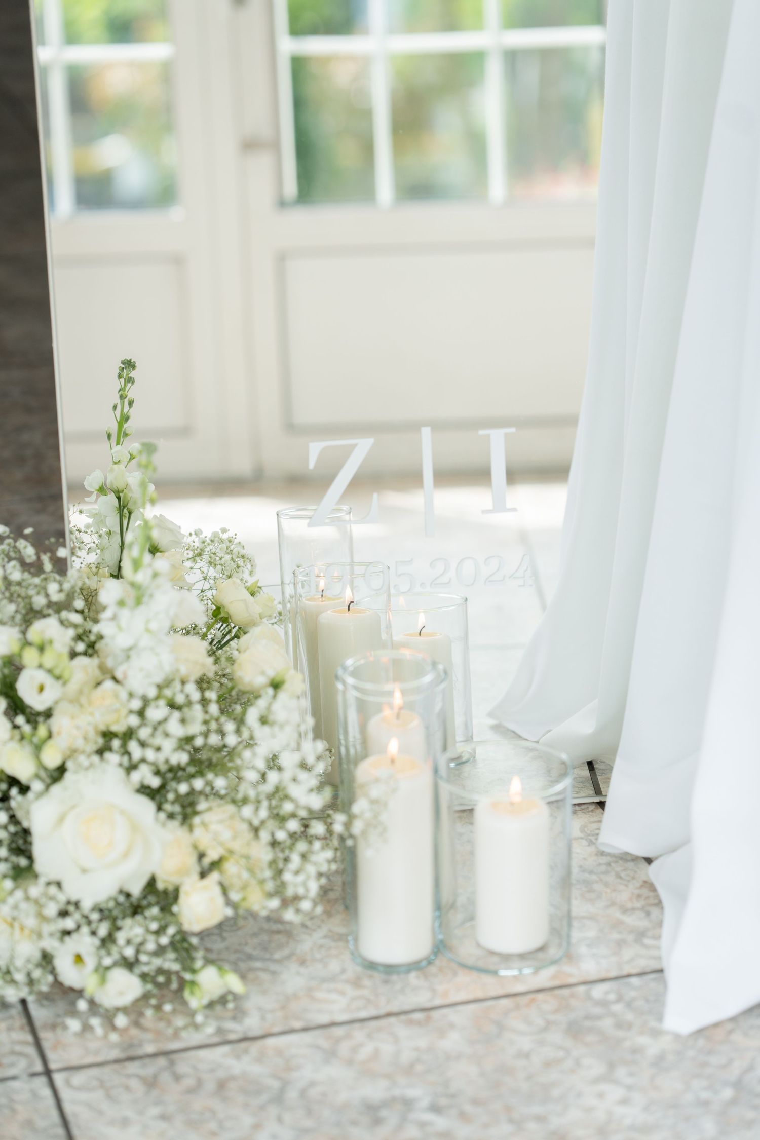 Elegant wedding decor featuring glowing white pillar candles and delicate baby's breath flowers by a bright window.