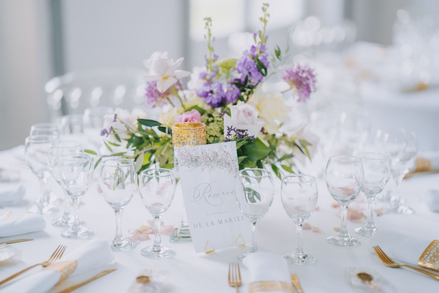 Elegant wedding table setting with purple floral centerpiece, wine glasses and formal place settings on white tablecloth.