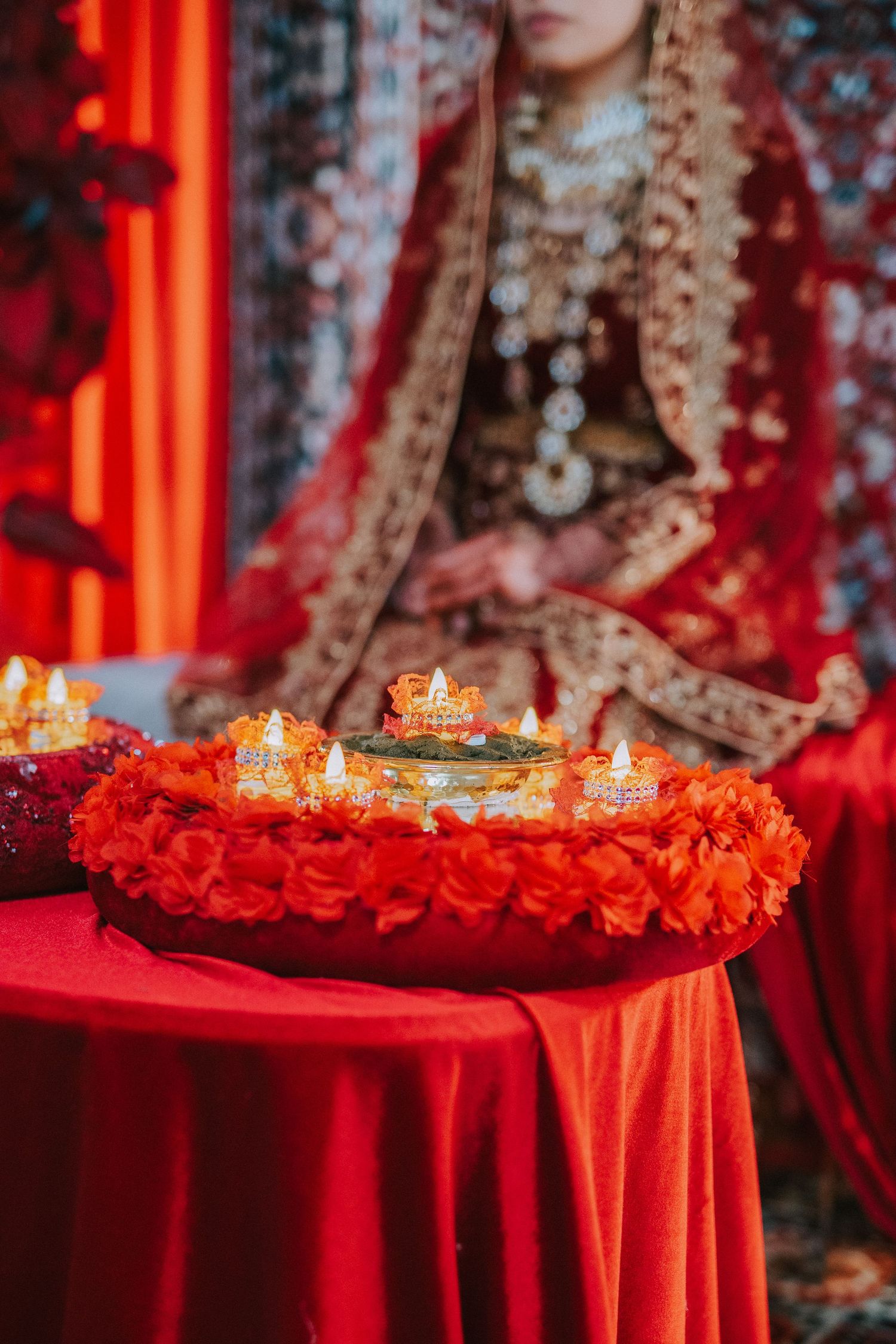 Lit candles on red table with traditional wedding decor and floral arrangements.