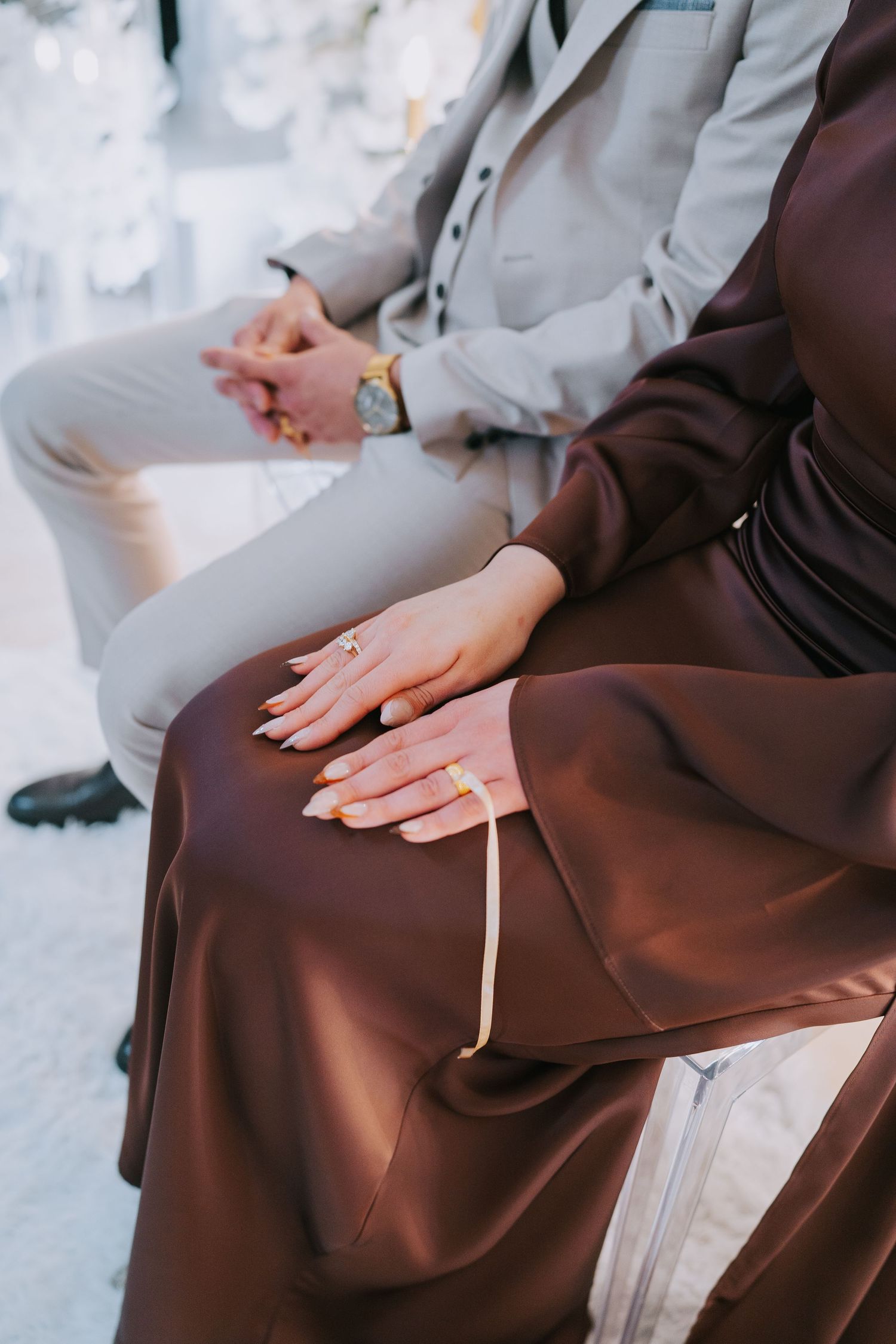 Hands resting on brown fabric with a grey suited person sitting nearby.