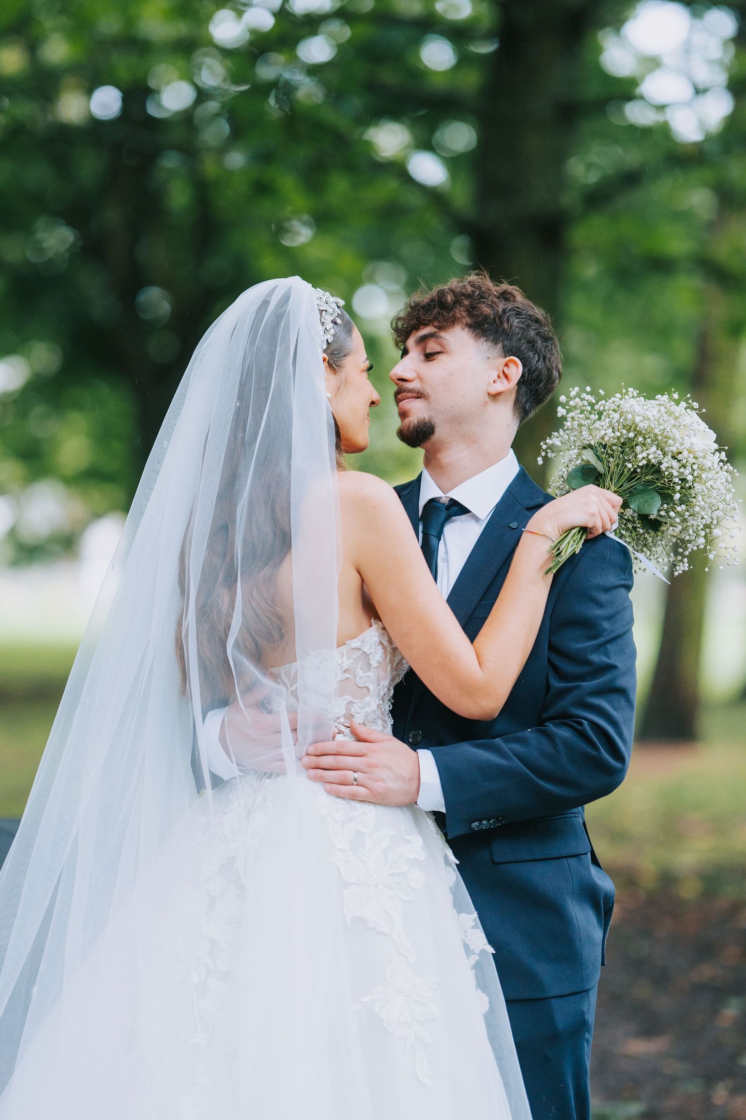 A romantic wedding portrait of a couple embracing outdoors with the bride in white dress holding baby's breath bouquet.