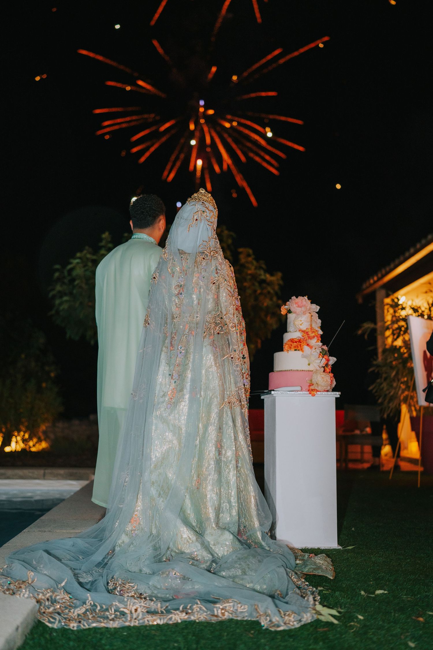 A couple admires fireworks during a wedding reception with their elegant wedding cake on display in the evening.