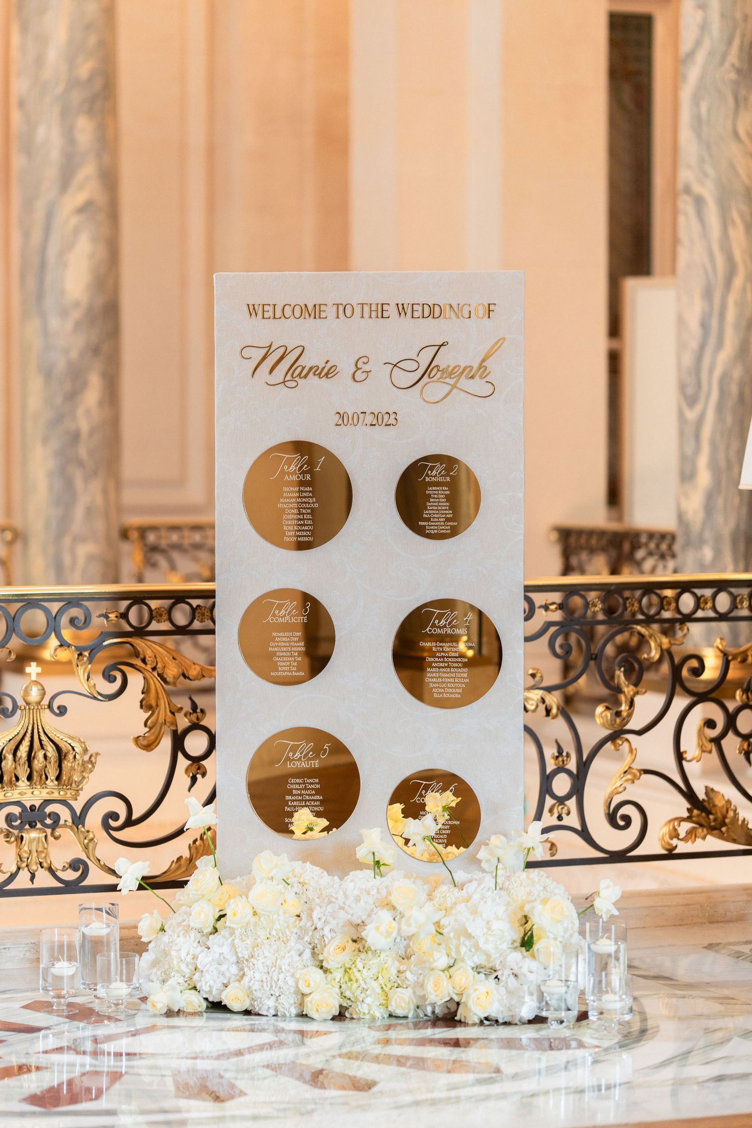 Elegant white and gold wedding welcome sign with circular timeline details displayed above white floral arrangements.