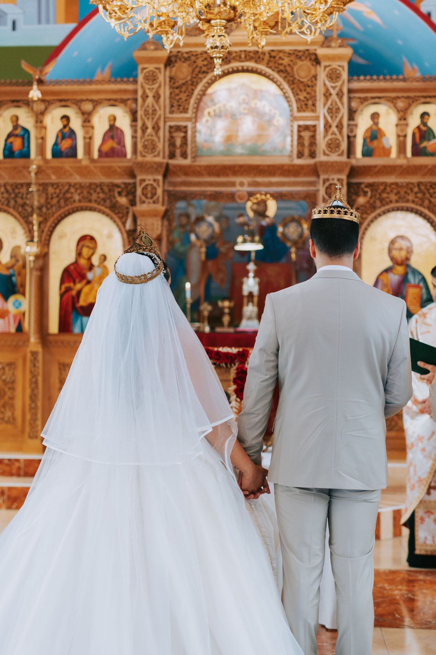 A couple stands at a church altar during an Orthodox Christian wedding ceremony in front of an ornate golden iconostasis.
