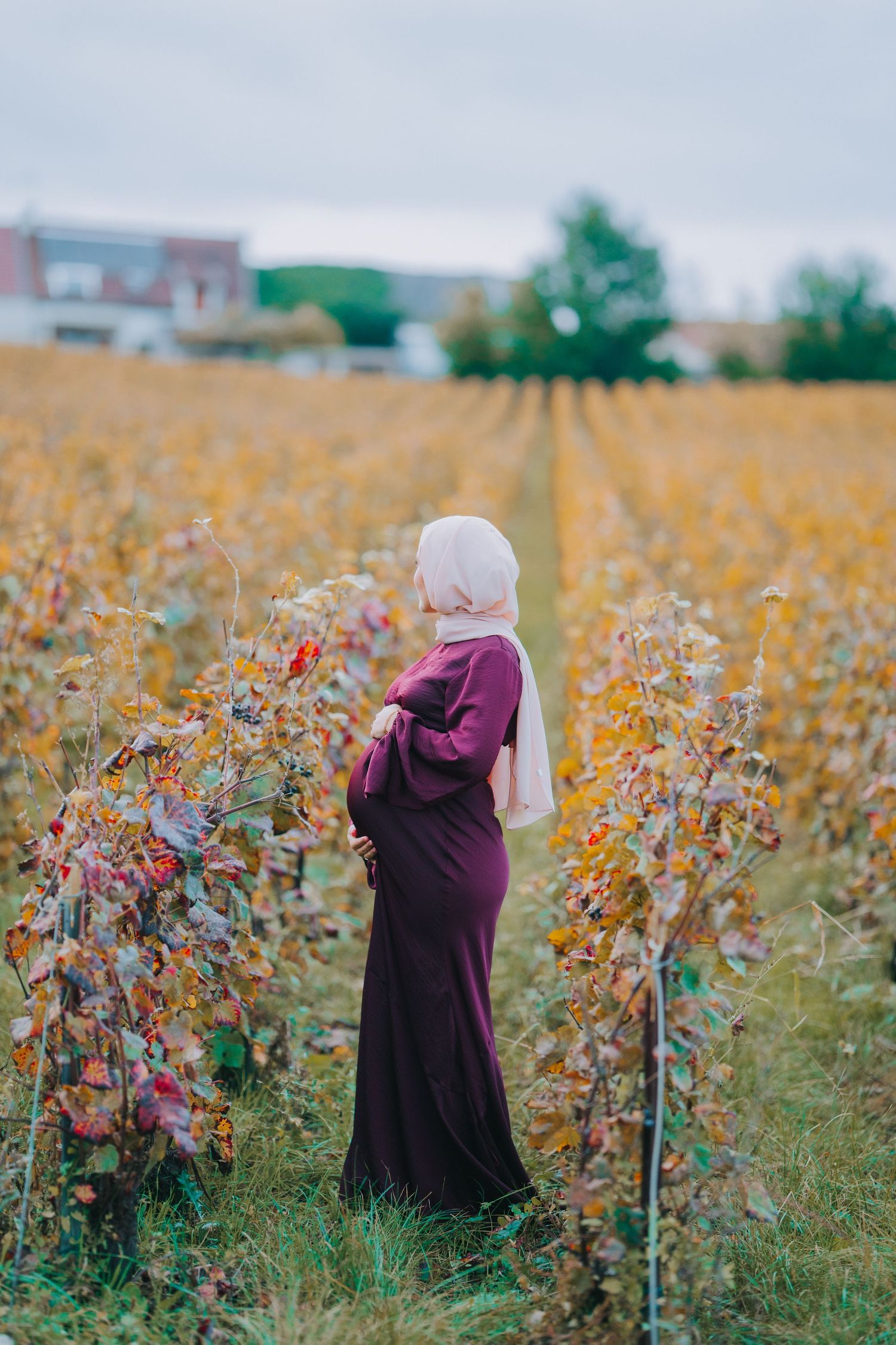 Figure in burgundy dress standing among autumn flowers in a scenic field.