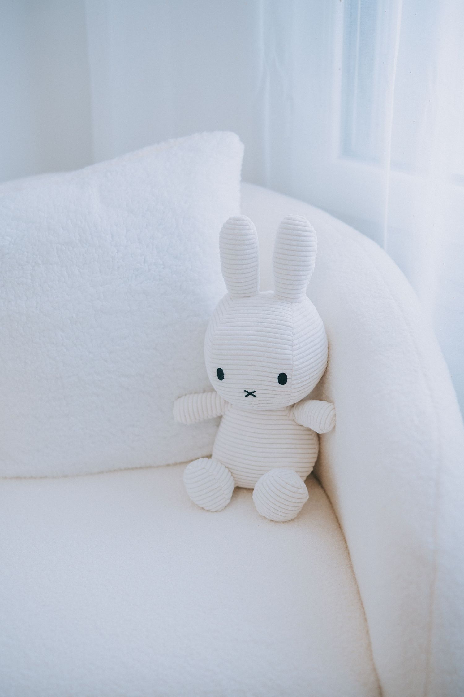 White stuffed bunny toy sitting alone on a pristine white couch.