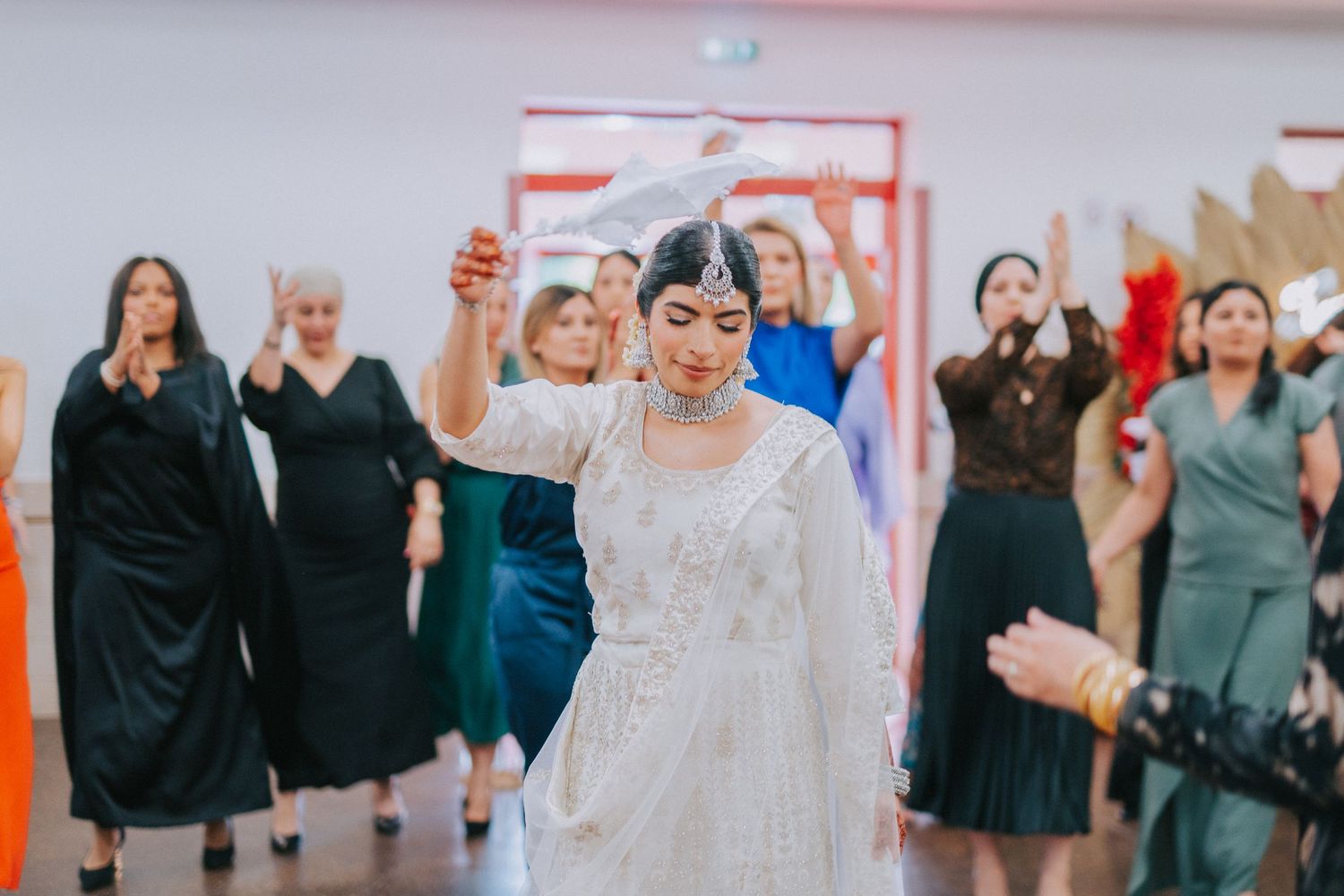 Wedding celebration with dancers in formal attire in a white reception hall.