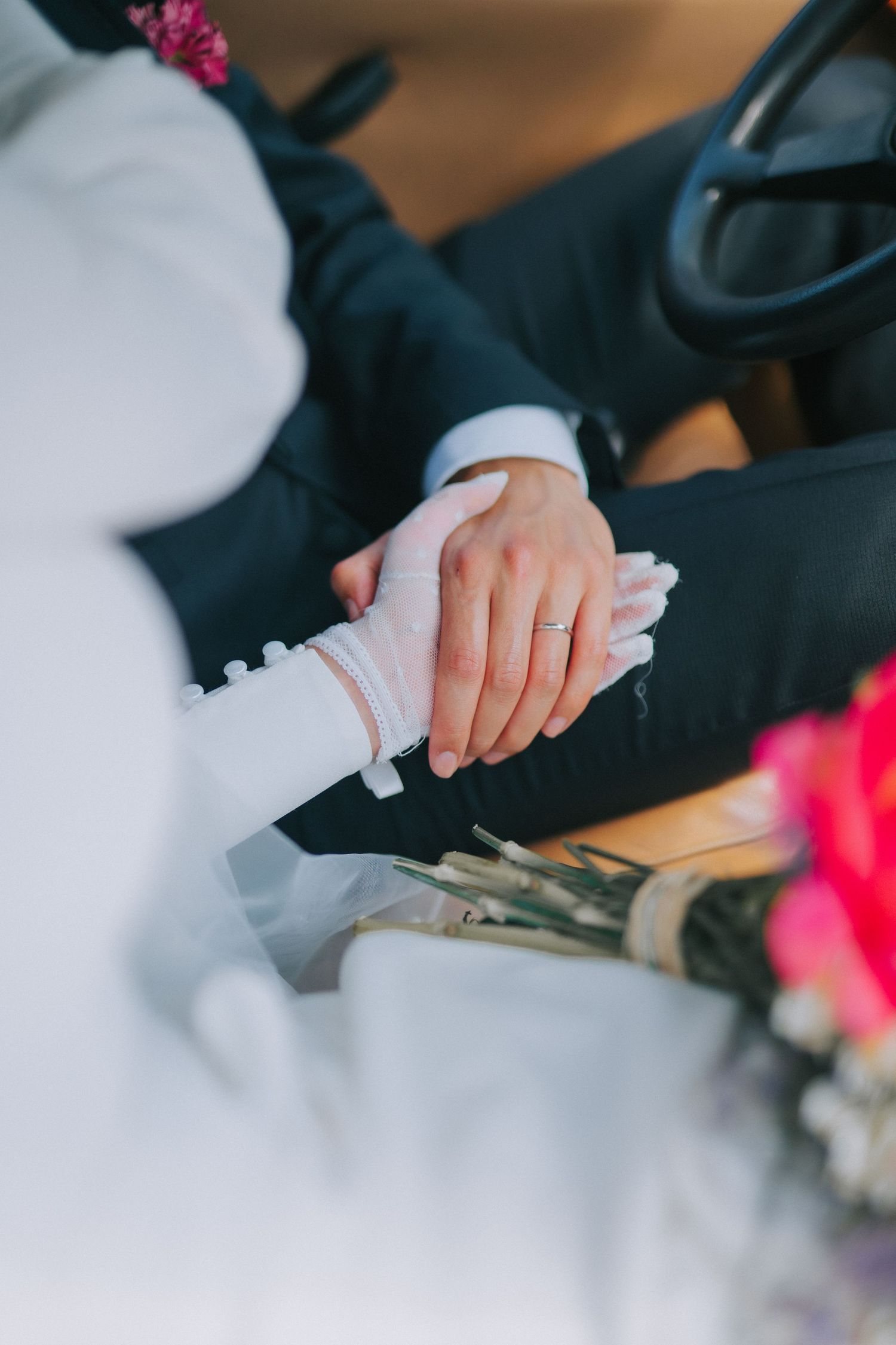 A close-up shot of hands holding together during a wedding ceremony, with white dress and dark suit visible.