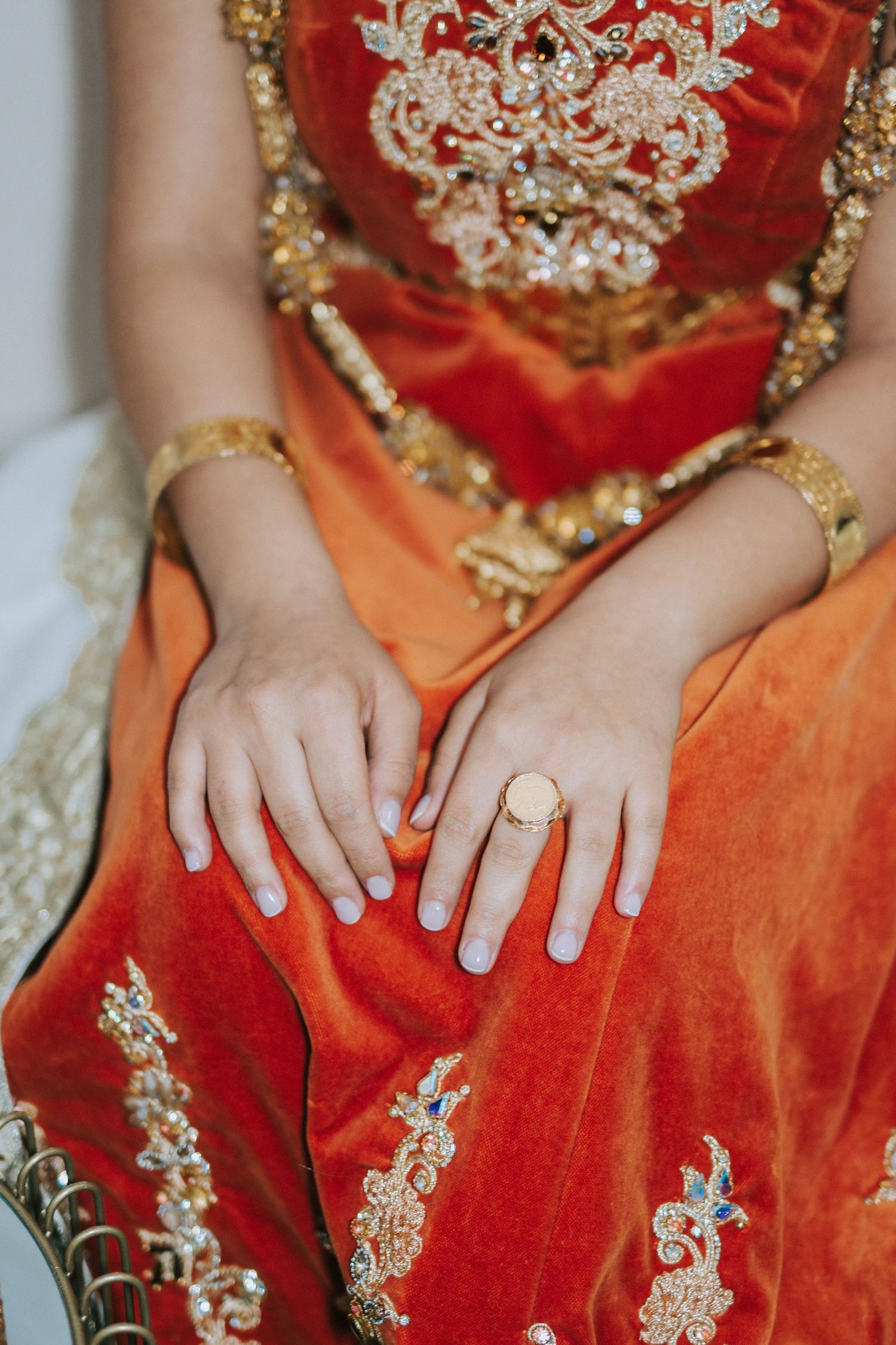 Close-up of hands resting on red embroidered dress showing wedding ring and traditional attire.