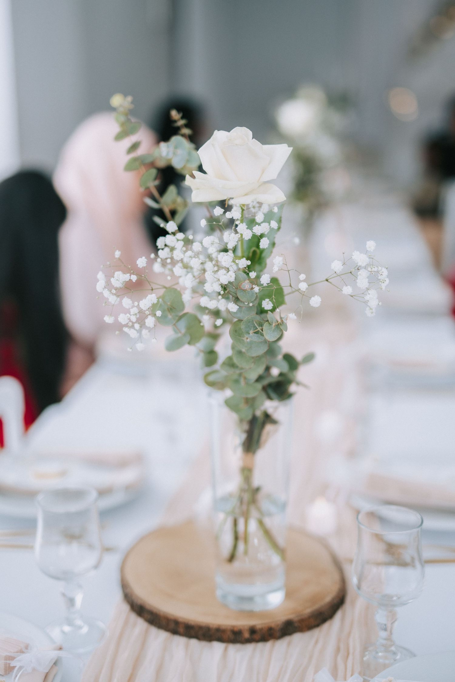 Elegant white rose and baby's breath centerpiece in glass vase on wooden slice.